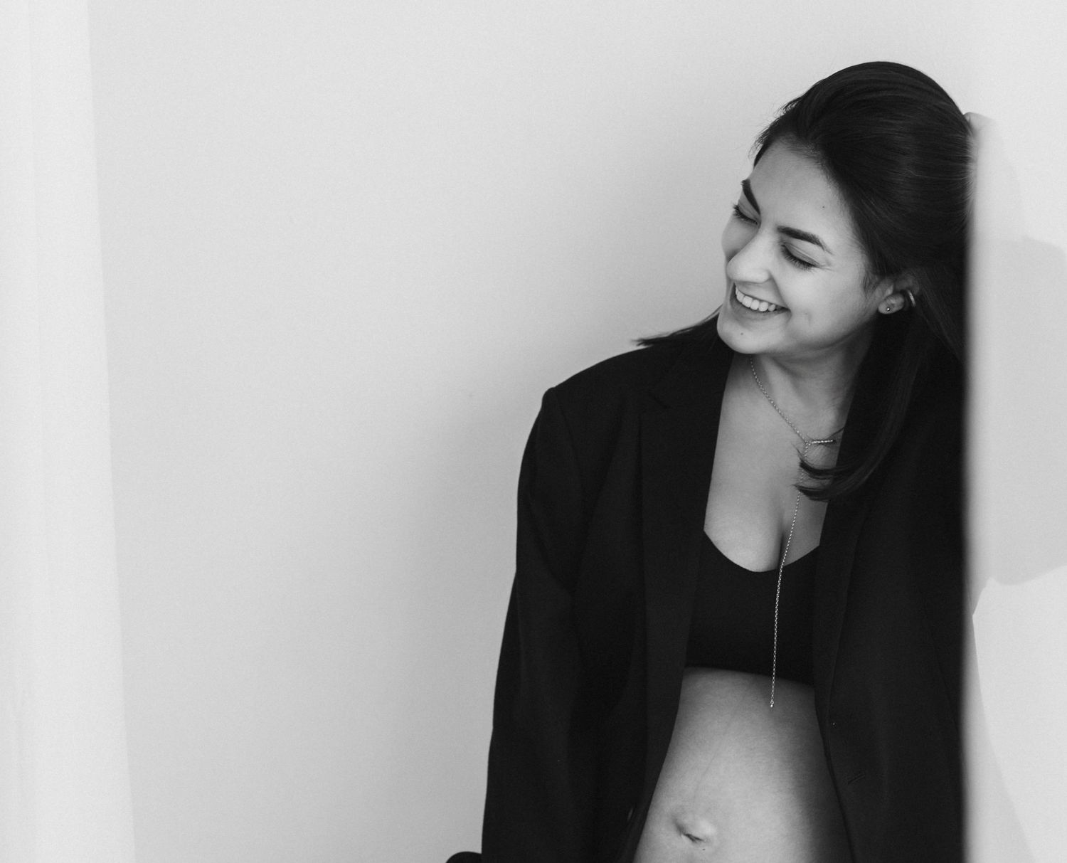 Black and white portrait of a woman in a blazer smiling against a white wall.