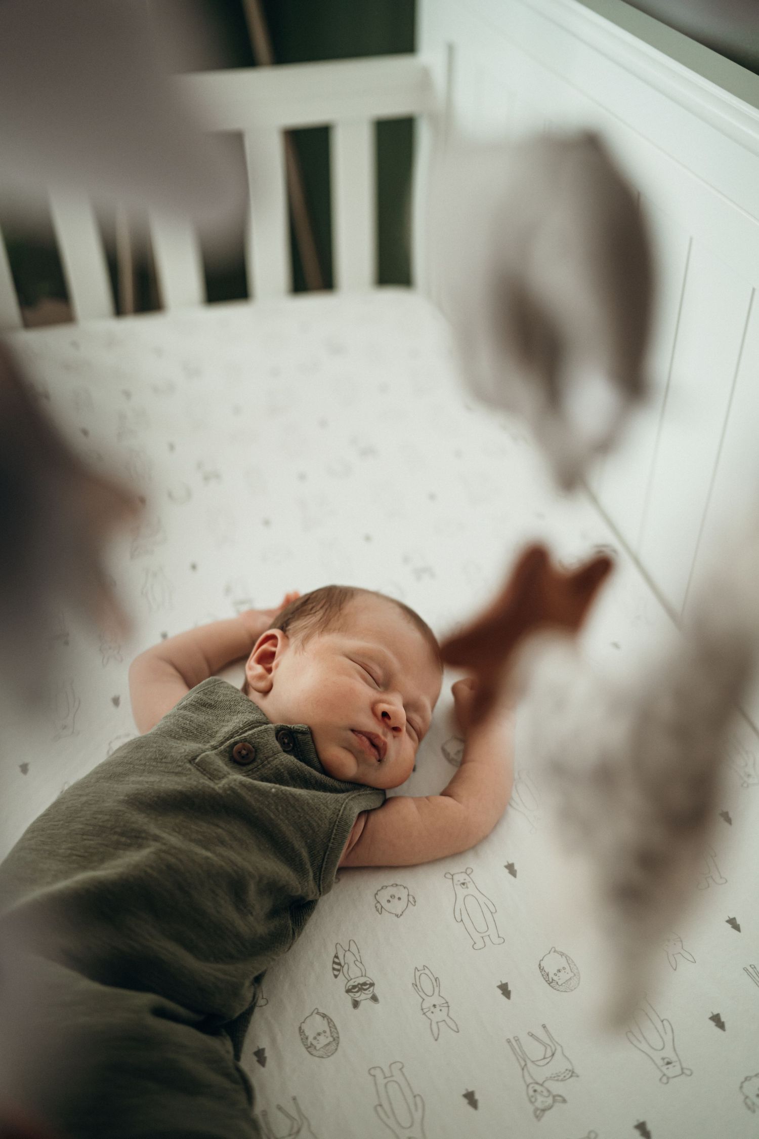 Baby sleeping peacefully in a crib with patterned sheets while wearing a green onesie.