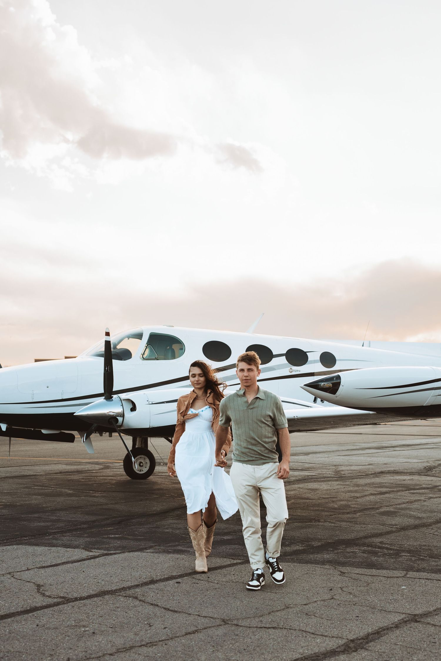 Couple walks together on airport tarmac at sunset next to private luxury aircraft.