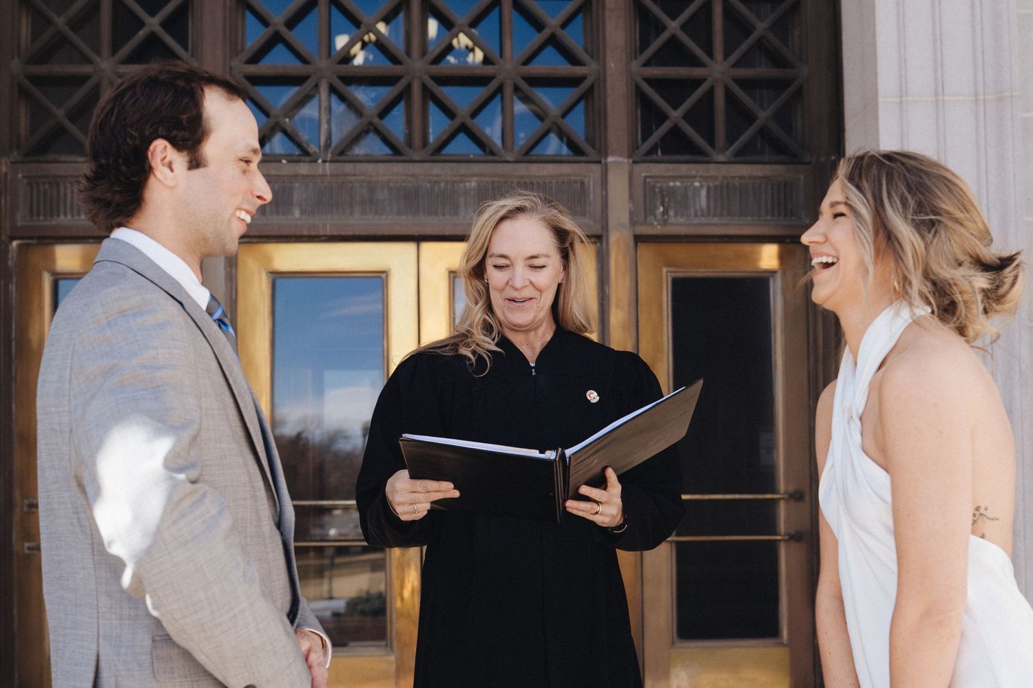 Two people share a joyful moment during an indoor wedding ceremony while holding papers.