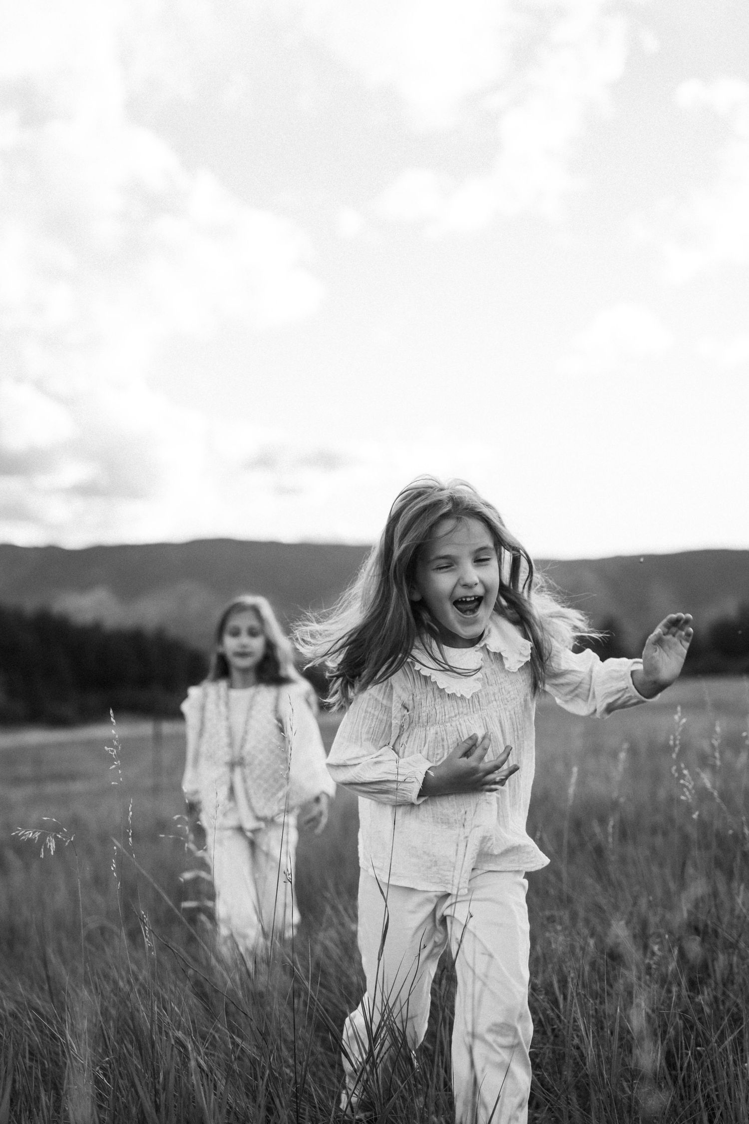 Black and white photo series showing joyful movement and dancing in a grassy meadow on an overcast day.