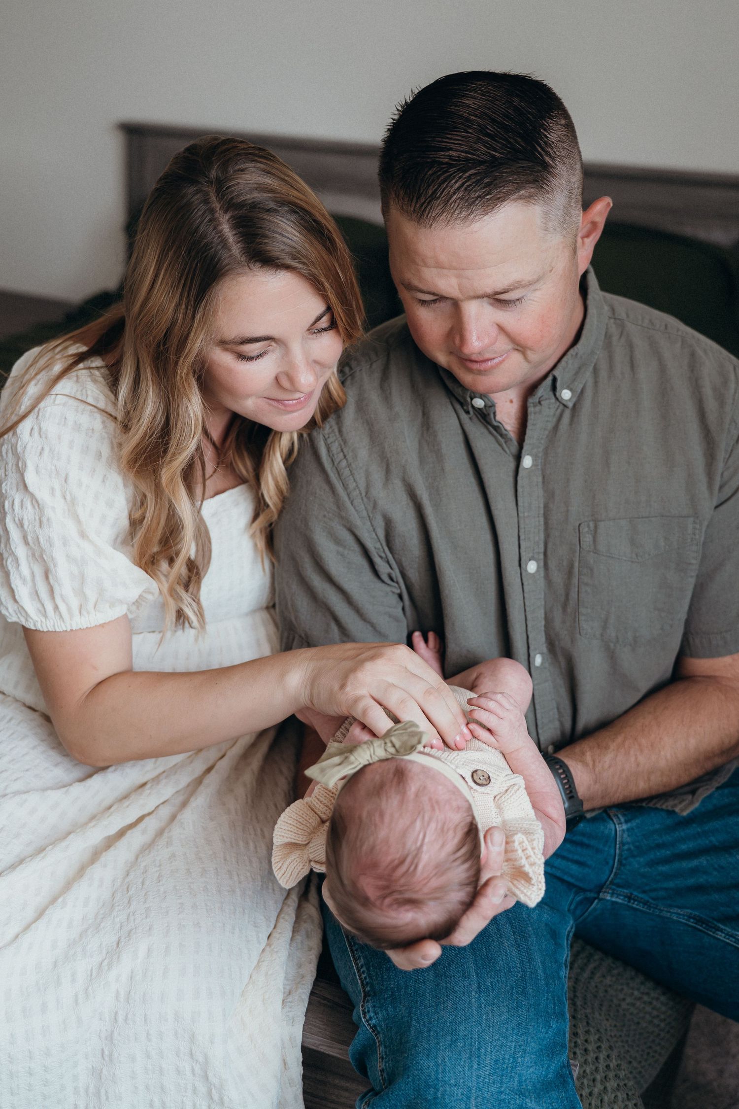 Parents in white and gray clothing share tender moments with their newborn baby in a series of intimate family portraits.