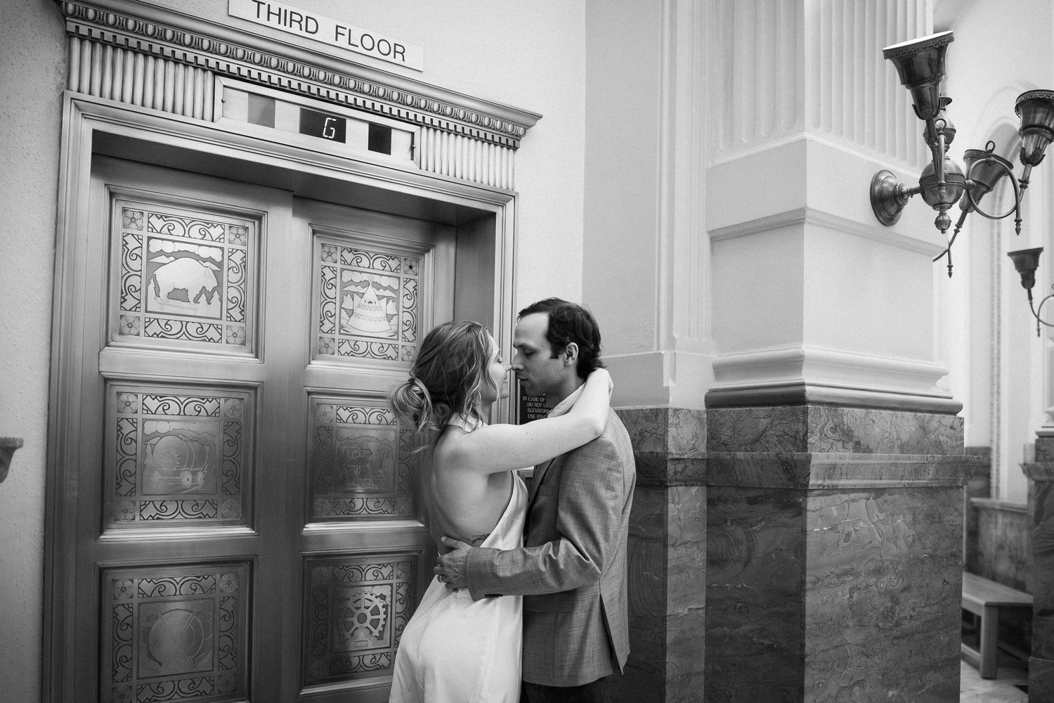 A romantic black and white moment between a couple sharing a kiss against an ornate vintage doorway.