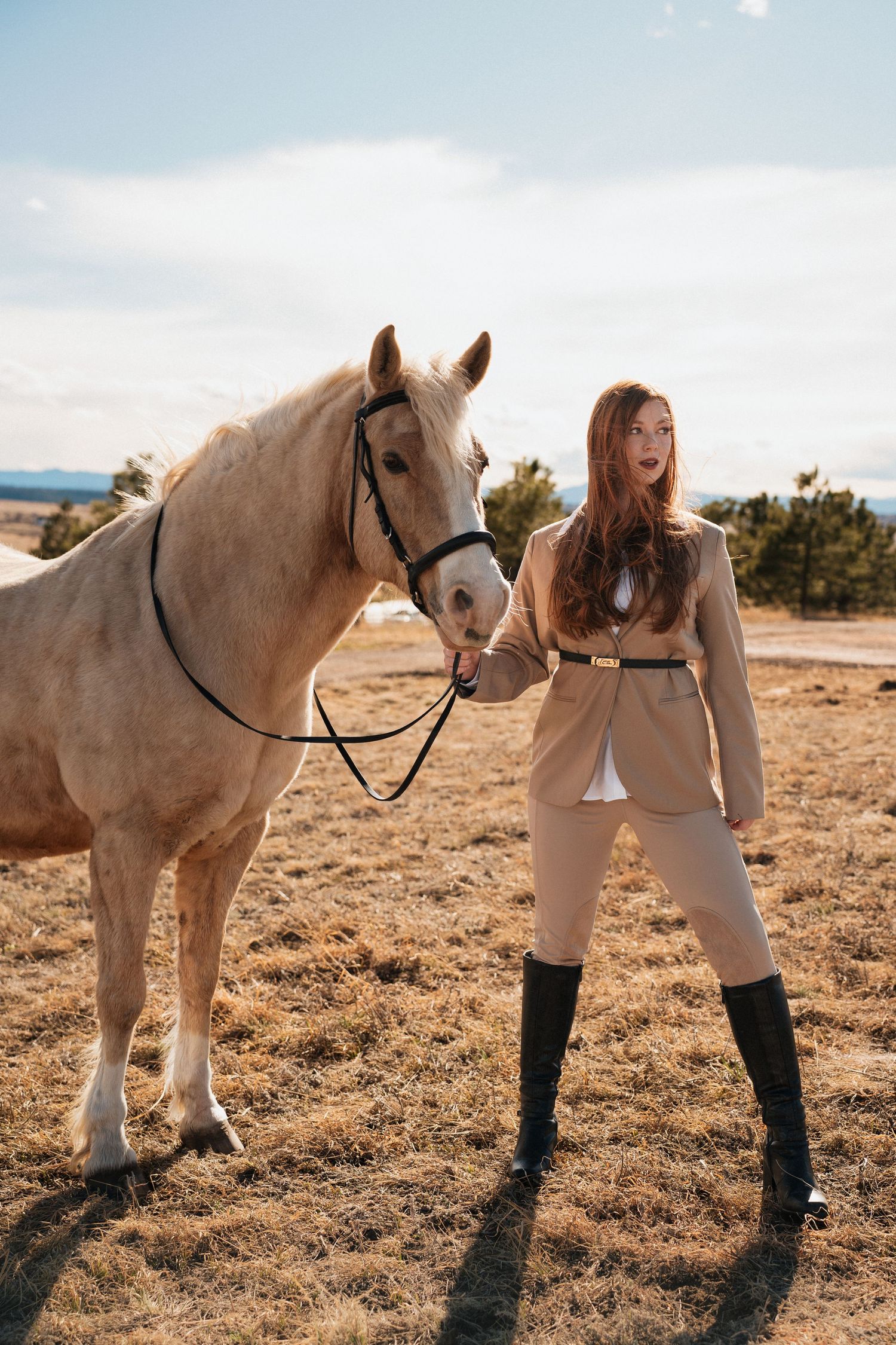 Beautiful white horse and rider in tan outfit and black boots pose together in a scenic desert landscape on a sunny day.