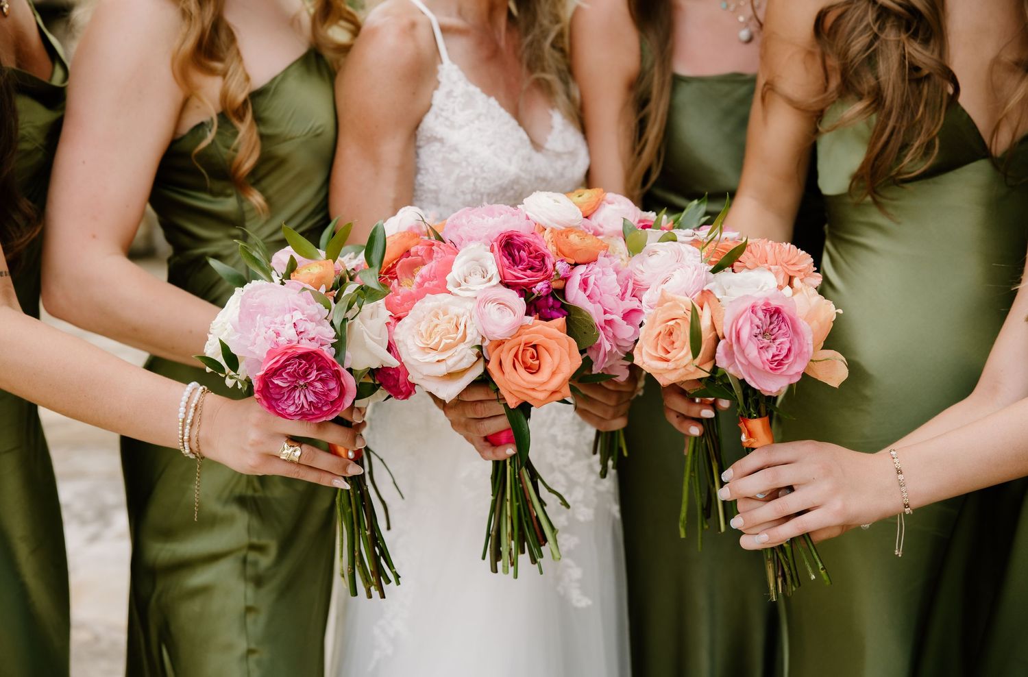 Bride and bridesmaids in olive green dresses holding vibrant pink, peach, and coral bouquets.
