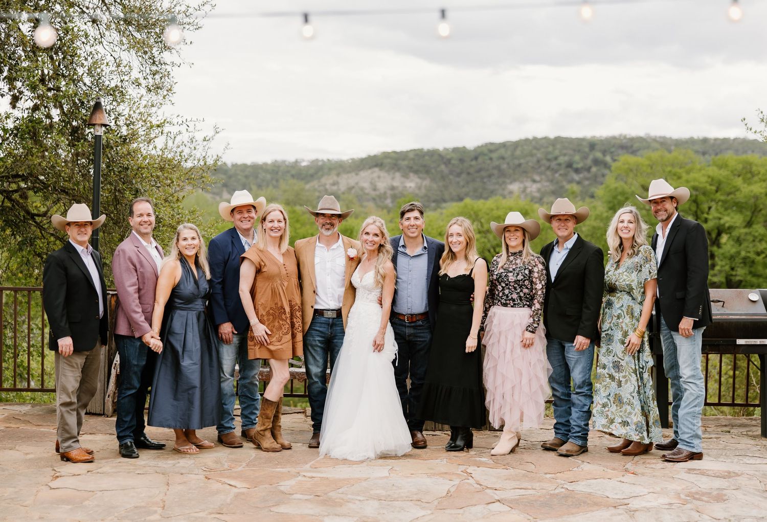 A wedding party group photo featuring the bride and groom surrounded by guests in cowboy hats on a stone patio.