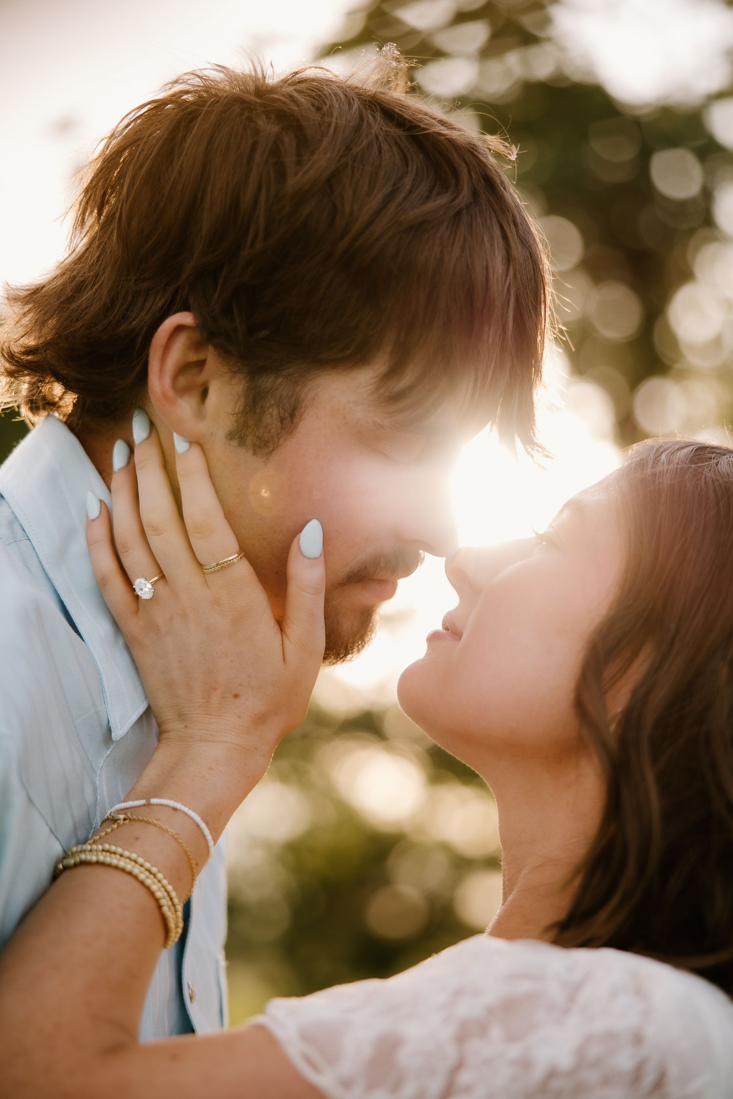 Couple sharing a tender forehead-to-forehead moment with golden bokeh sunset background.