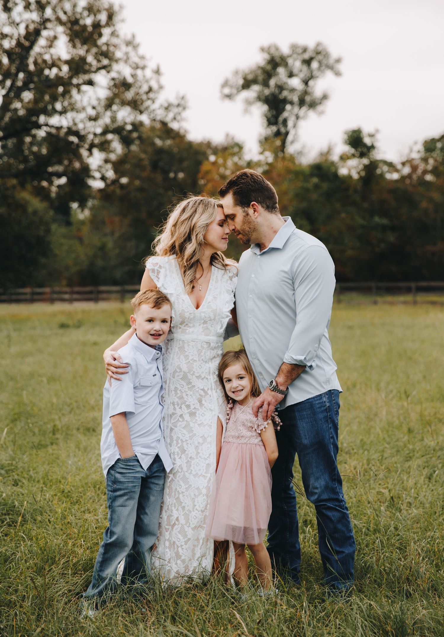 Family of four posing in a green field, parents gazing at each other while children smile at the camera.