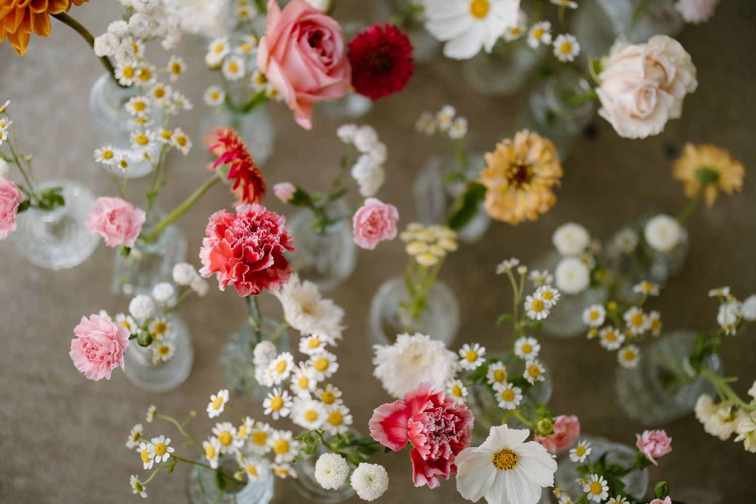 Elegant floral arrangement featuring pink roses, carnations, daisies, and wildflowers in clear glass vases.