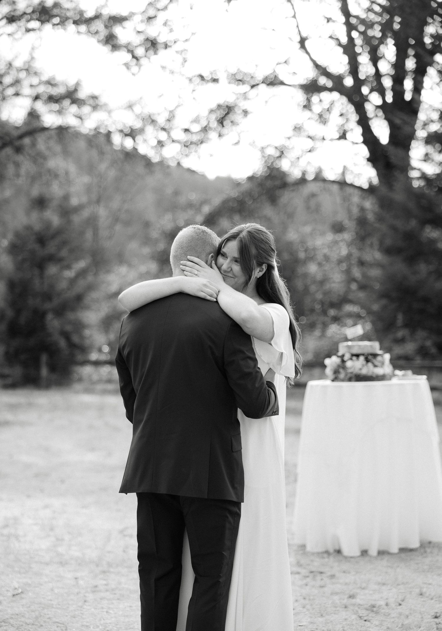 Black and white photo of bride and groom embracing tenderly at outdoor wedding reception.