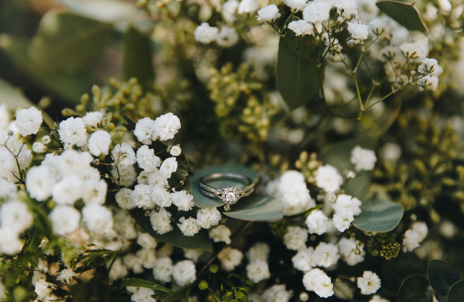 Diamond engagement ring nestled in a bridal bouquet of white baby's breath and eucalyptus.