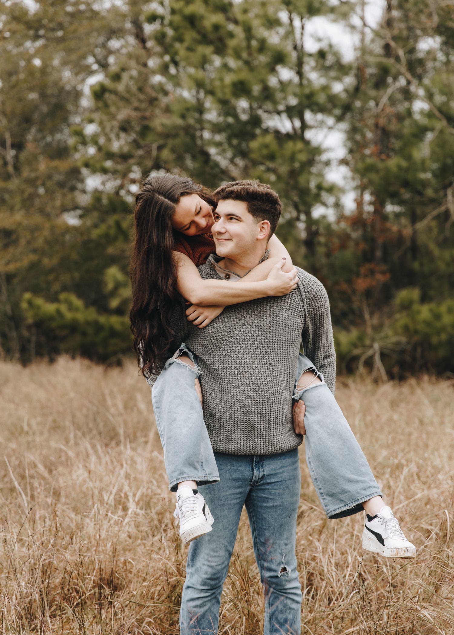Happy young man giving his girlfriend a piggyback ride in a dry grass field.