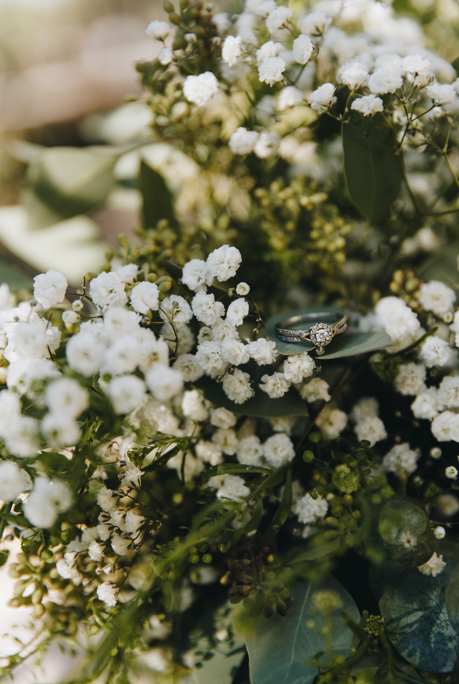 Close-up of a diamond engagement ring nestled in a lush bouquet of white baby's breath flowers.