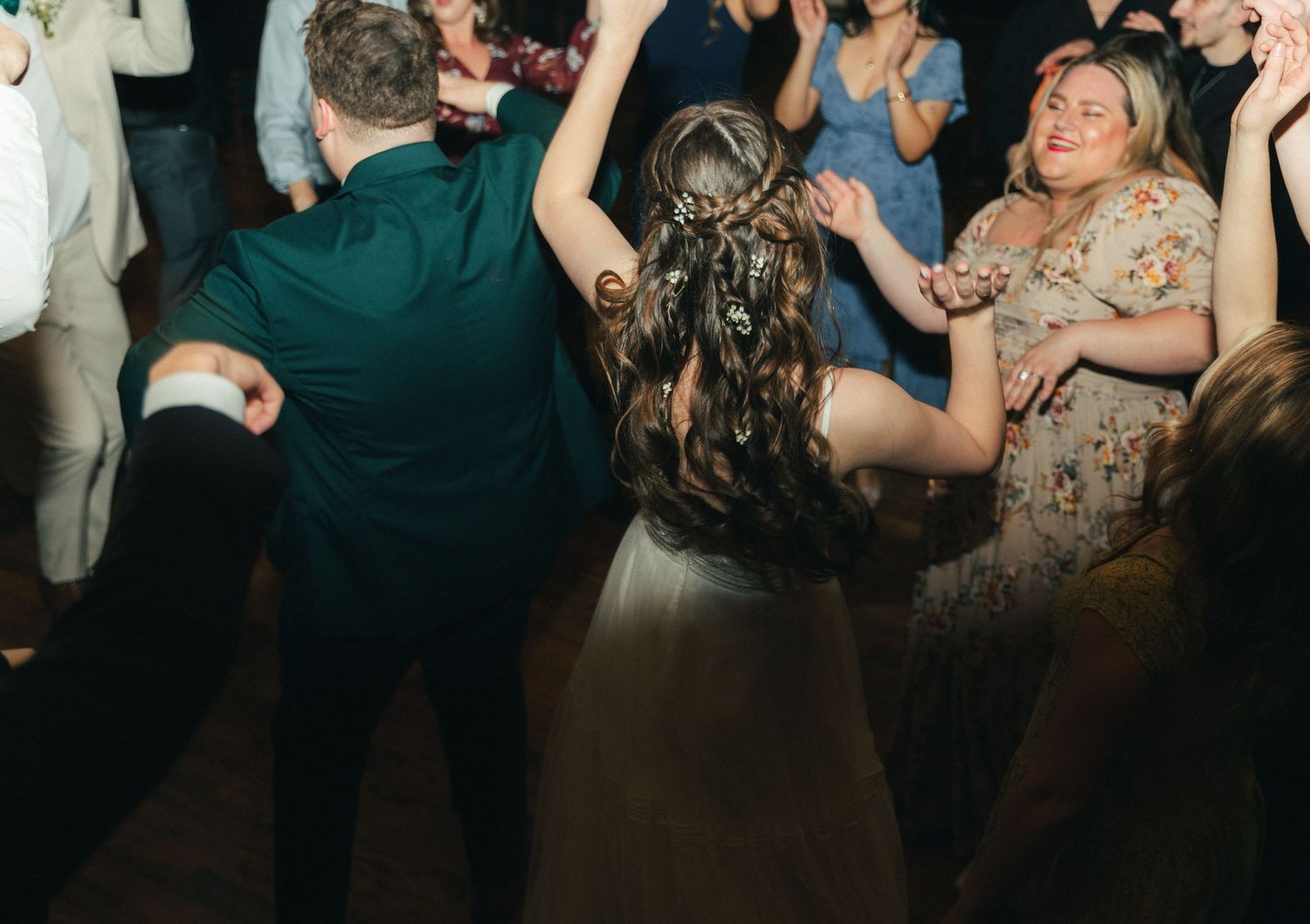 Bride dances joyfully with wedding guests on a crowded dance floor during lively wedding reception.
