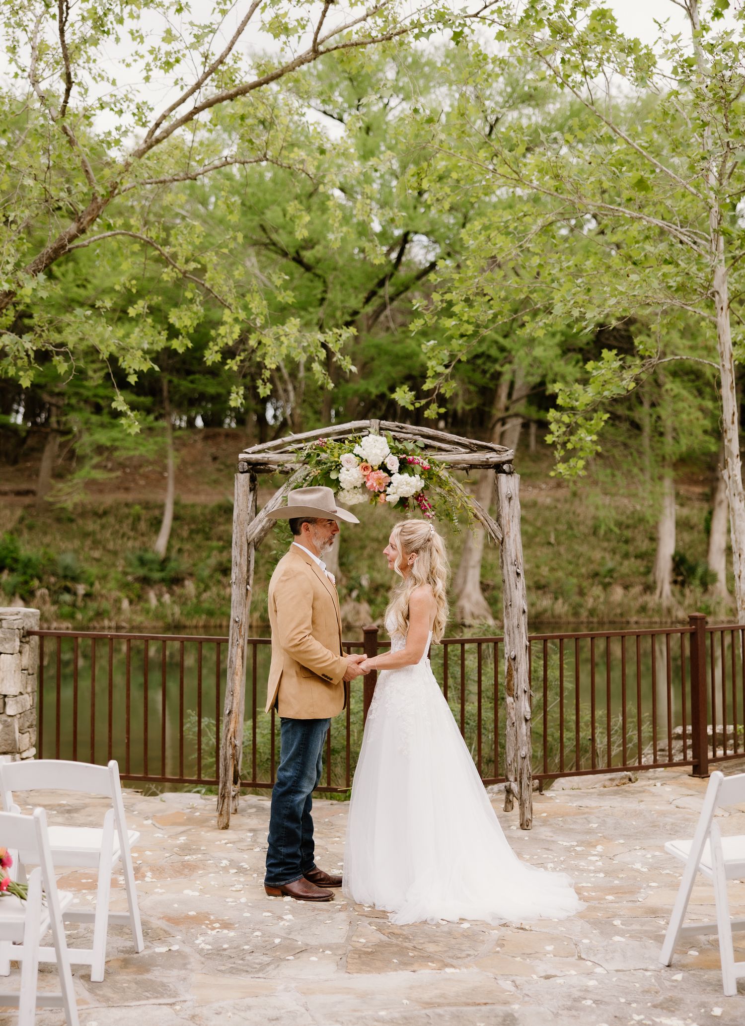Bride and groom holding hands under rustic wooden arch at outdoor ceremony.