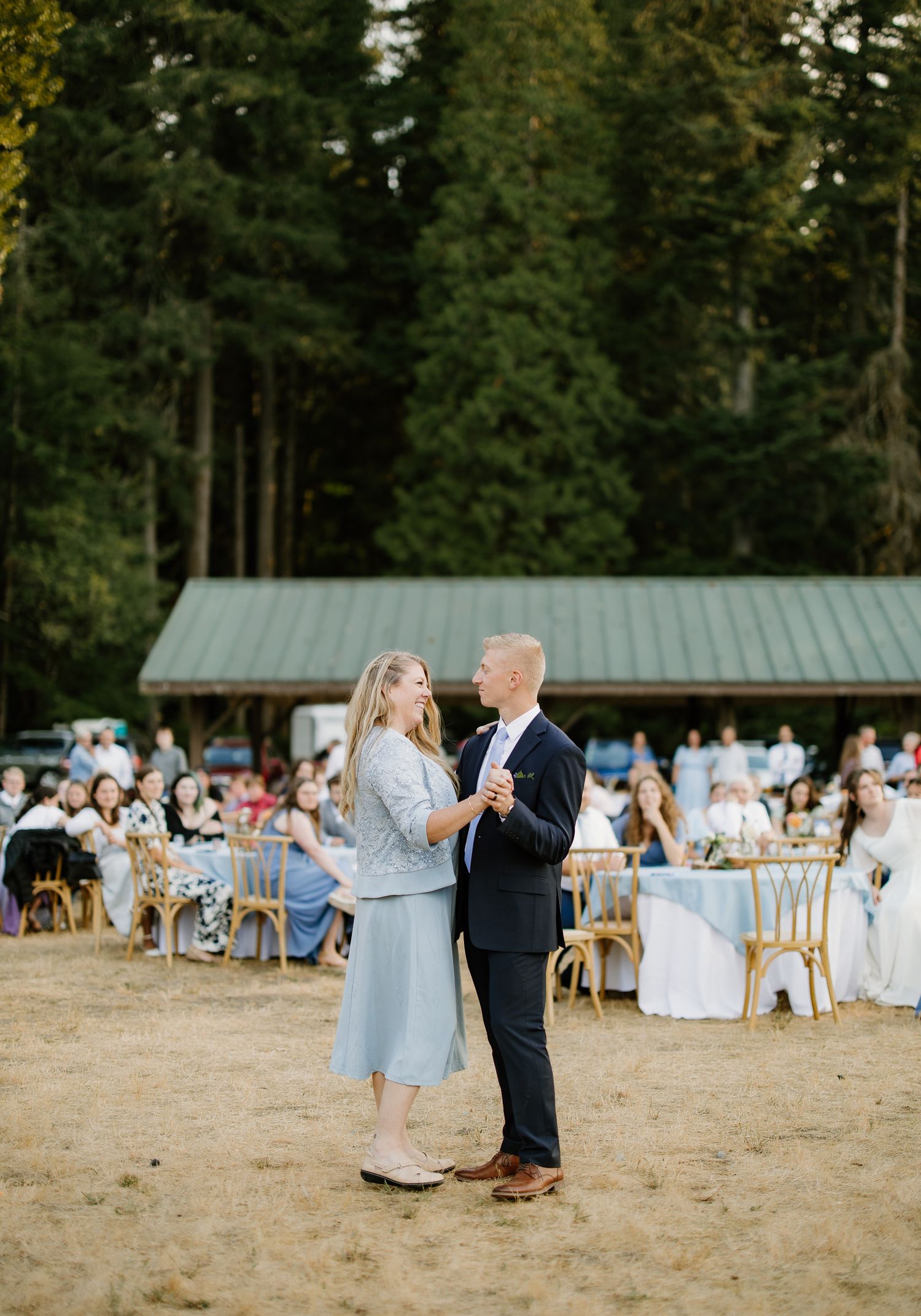 Couple shares first dance on sandy outdoor floor with wedding guests seated behind.