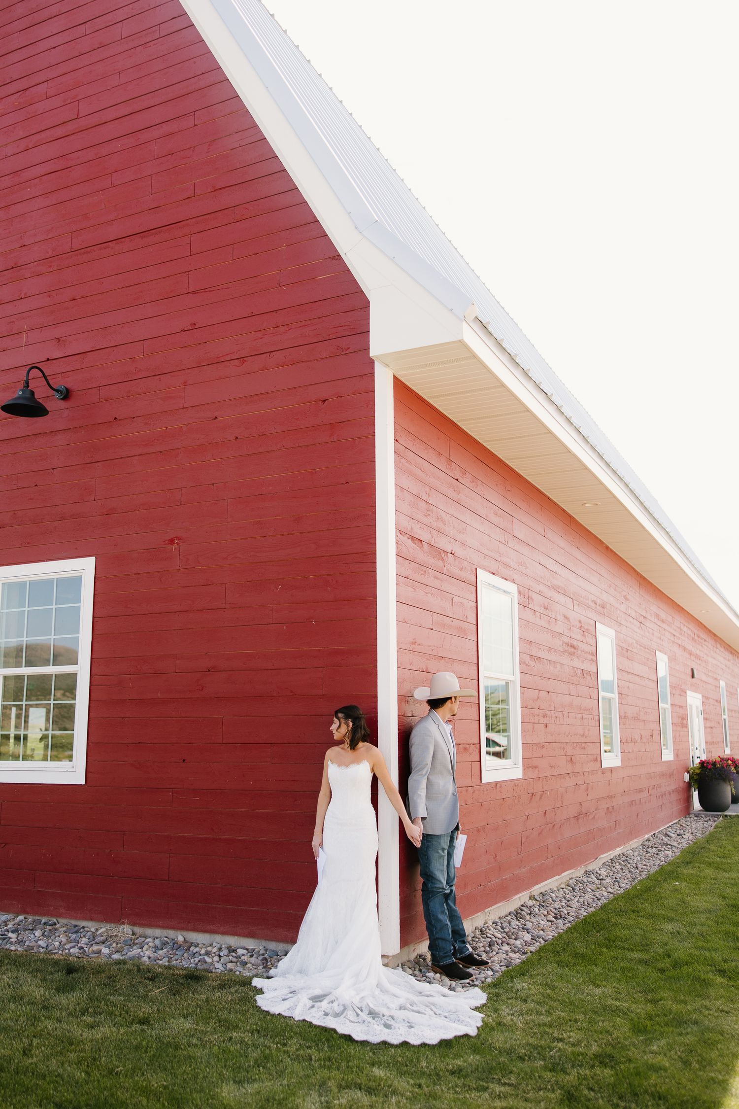 Bride and groom holding hands outside a red barn wedding venue, bride in elegant white gown with long train.