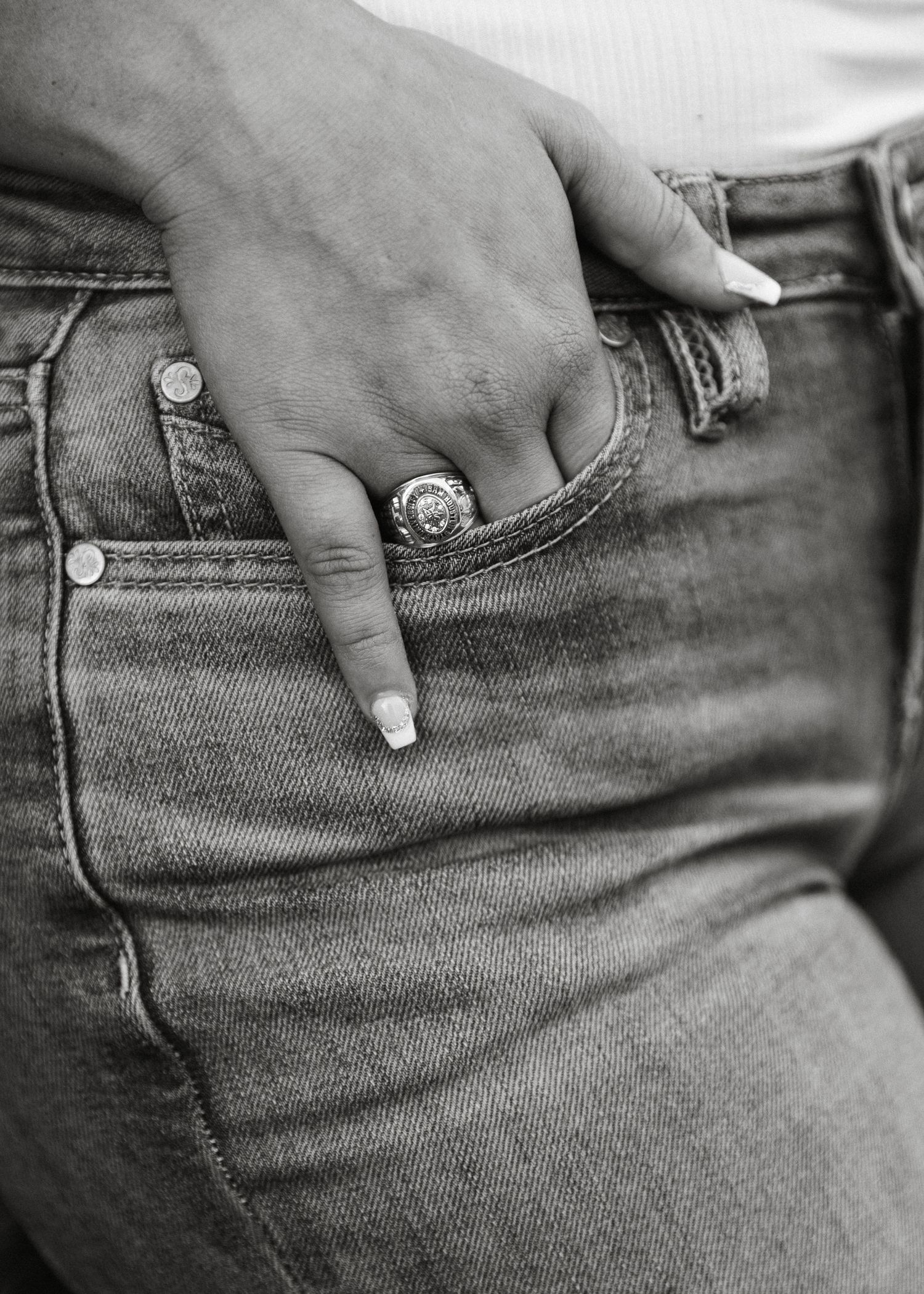 Close-up black and white photo of a hand with a ring tucked into the pocket of light wash jeans.