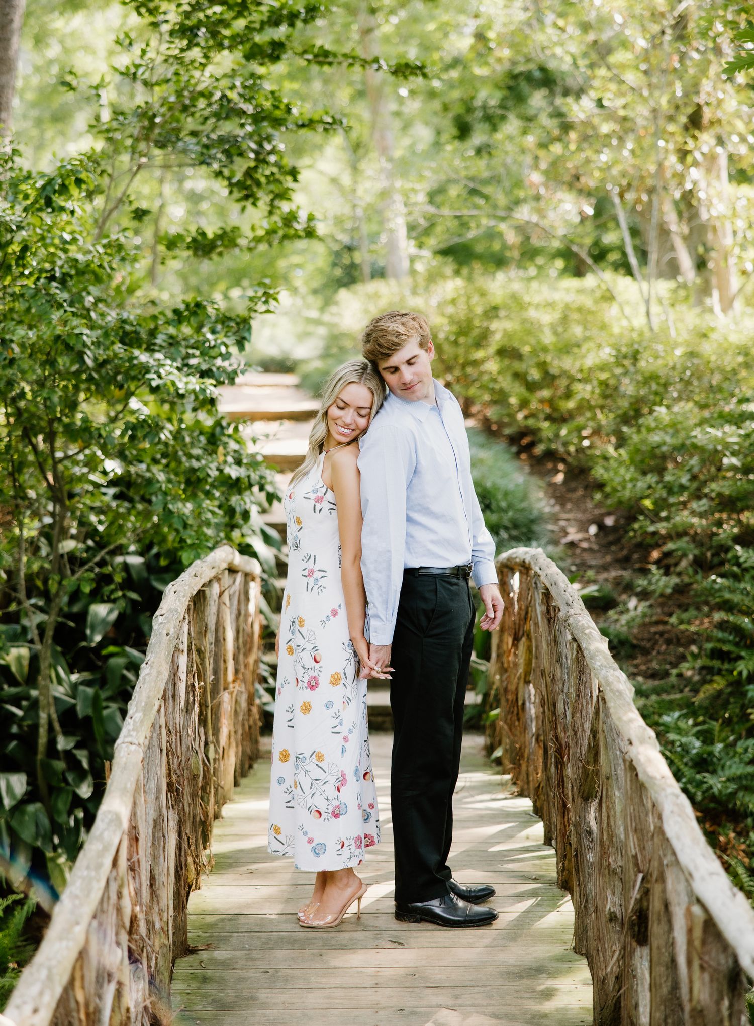 Couple holding hands on a rustic wooden bridge surrounded by lush green foliage.