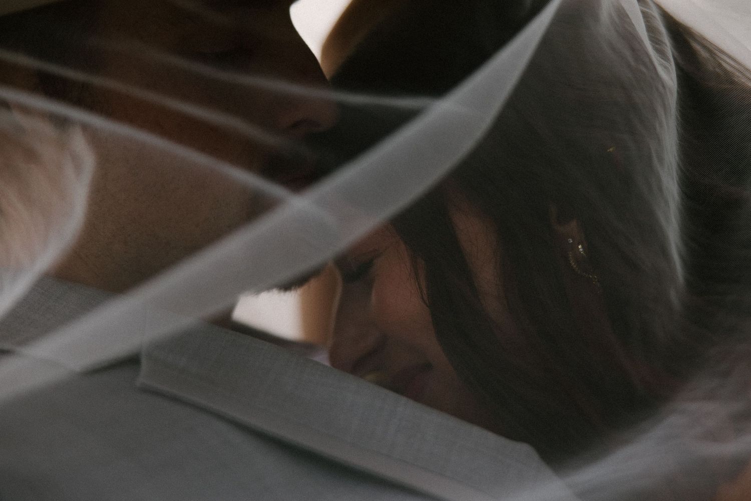 Intimate close-up of bride and groom under a flowing veil.