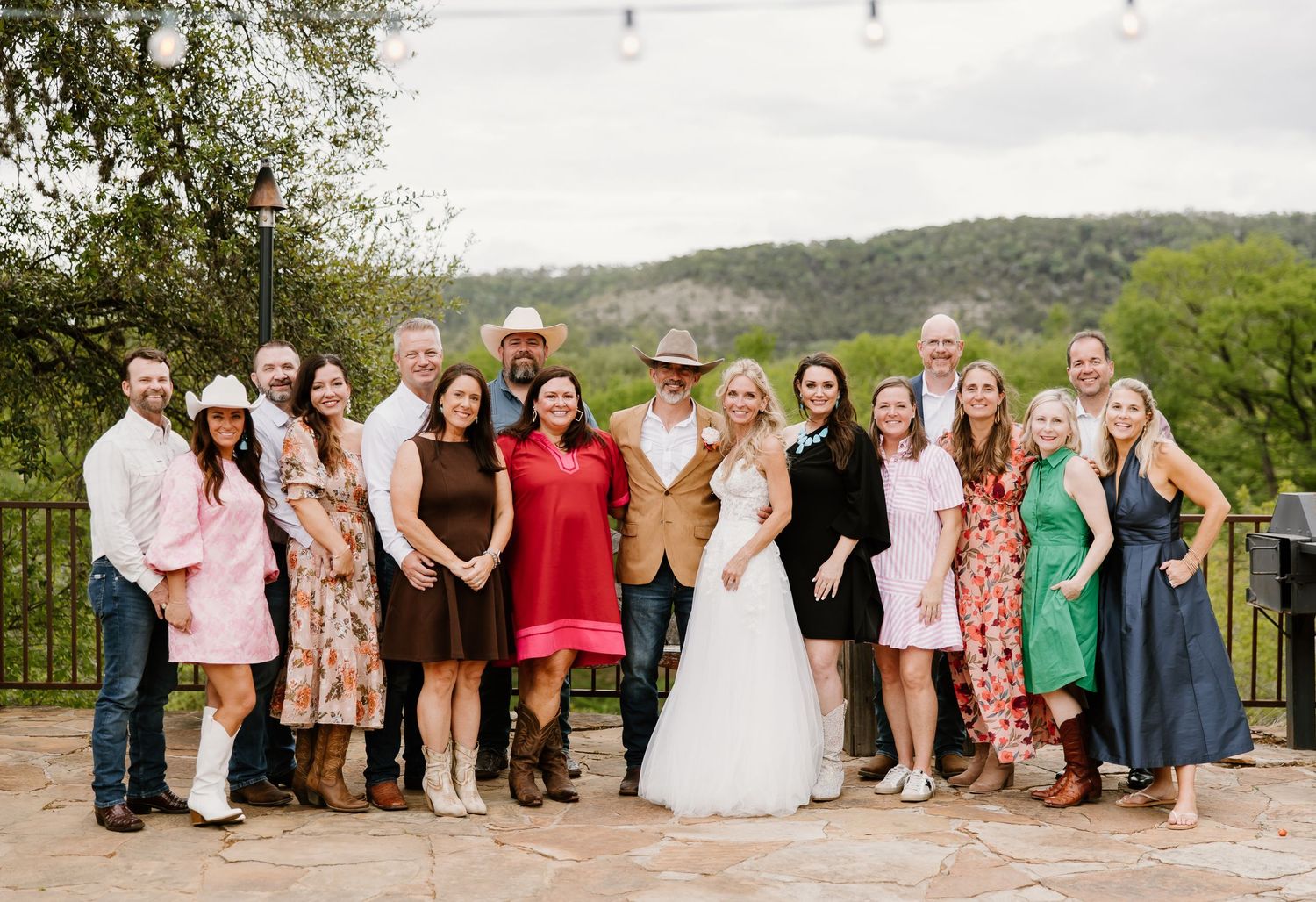 Wedding party and guests posing together outdoors with scenic hill country views in the background.