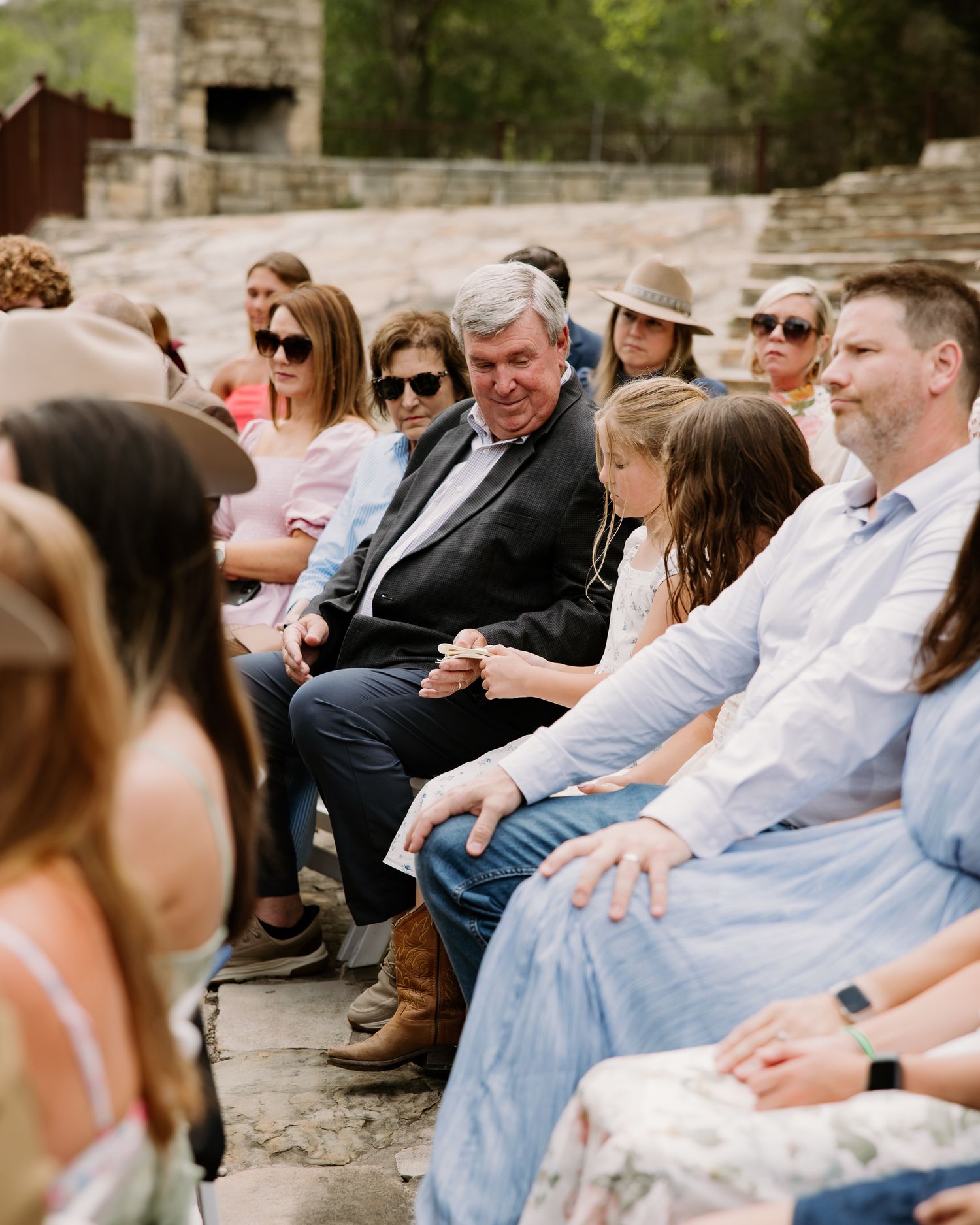 Wedding guests seated outdoors smiling and enjoying rustic countryside ceremony.