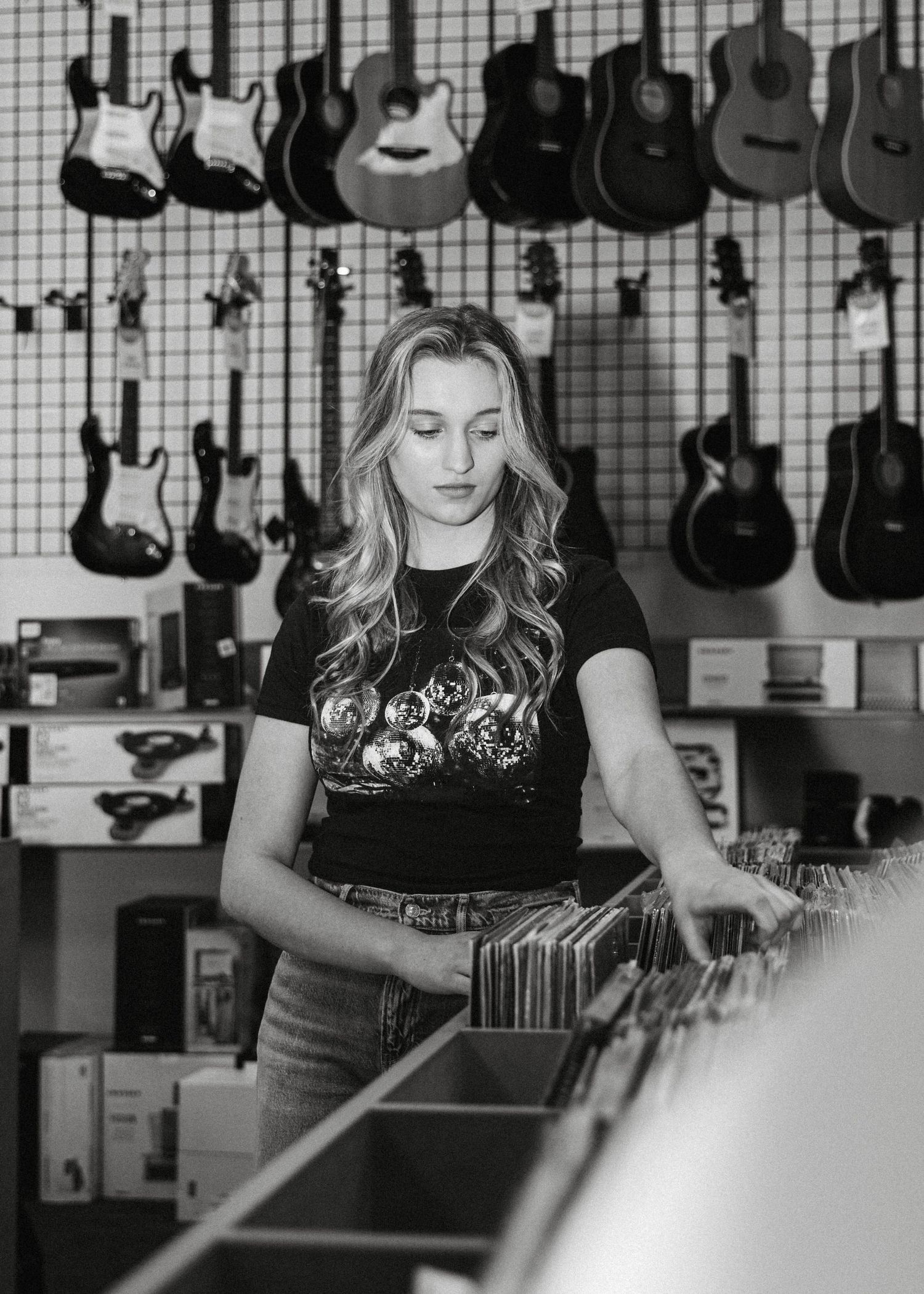 Blonde woman browsing vinyl records in guitar shop in black and white music-themed senior portrait photo.
