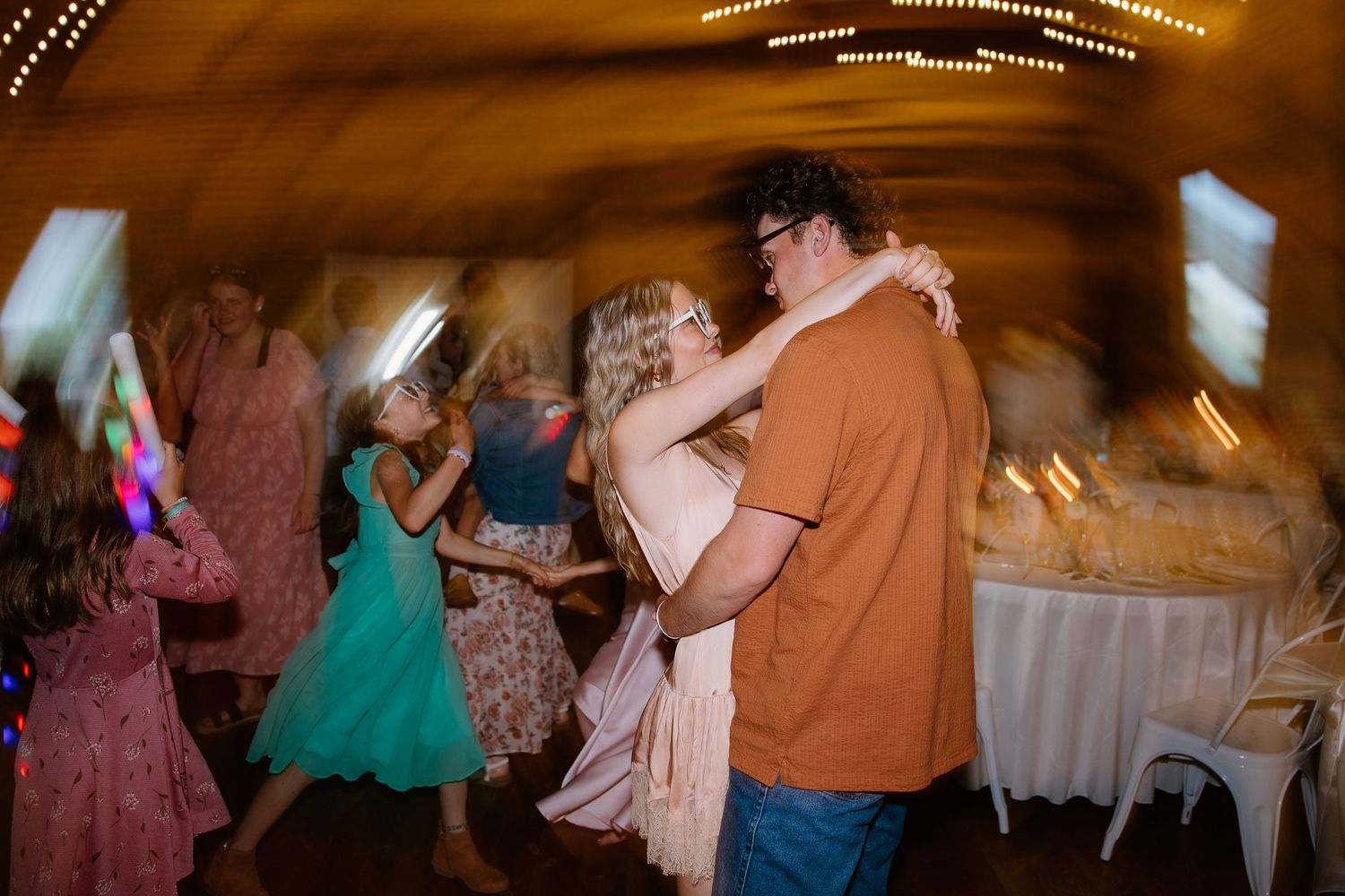Couple shares a romantic dance embrace on a blurred, warmly lit wedding reception dance floor.