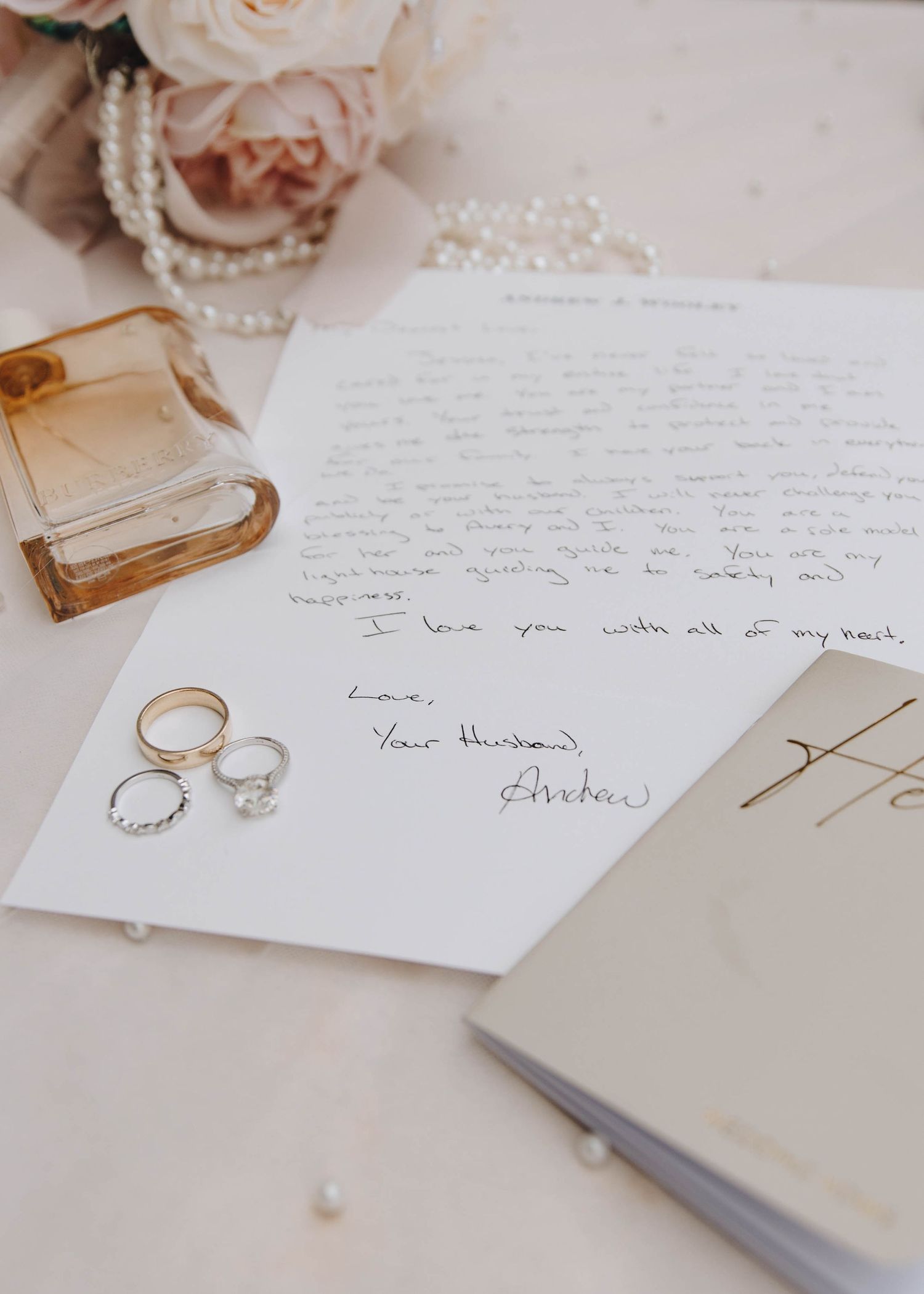 Wedding detail flat lay with handwritten love letter signed Your Husband, rings, and perfume bottle.