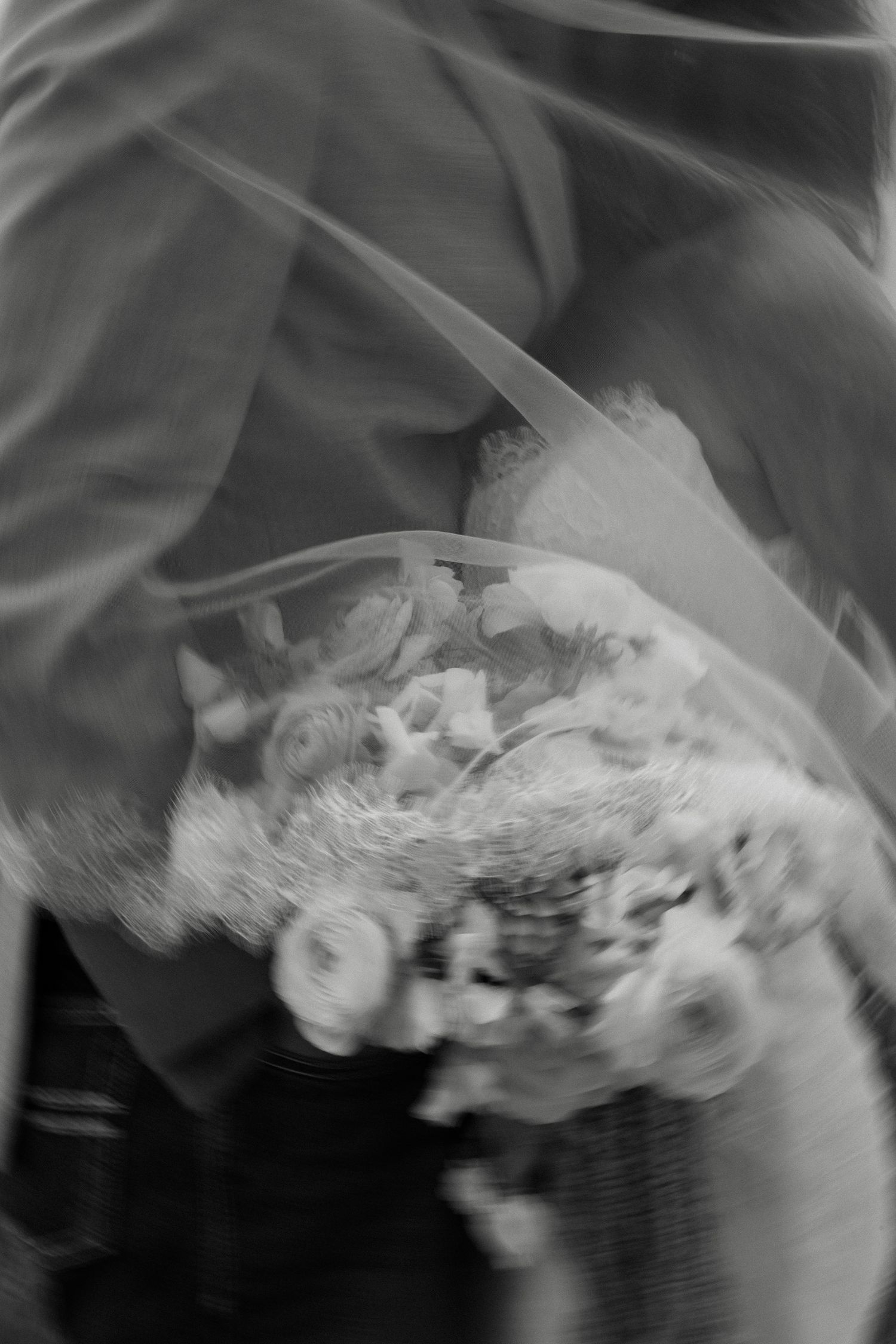 Blurred black and white close-up of bridal bouquet with roses under wedding veil.
