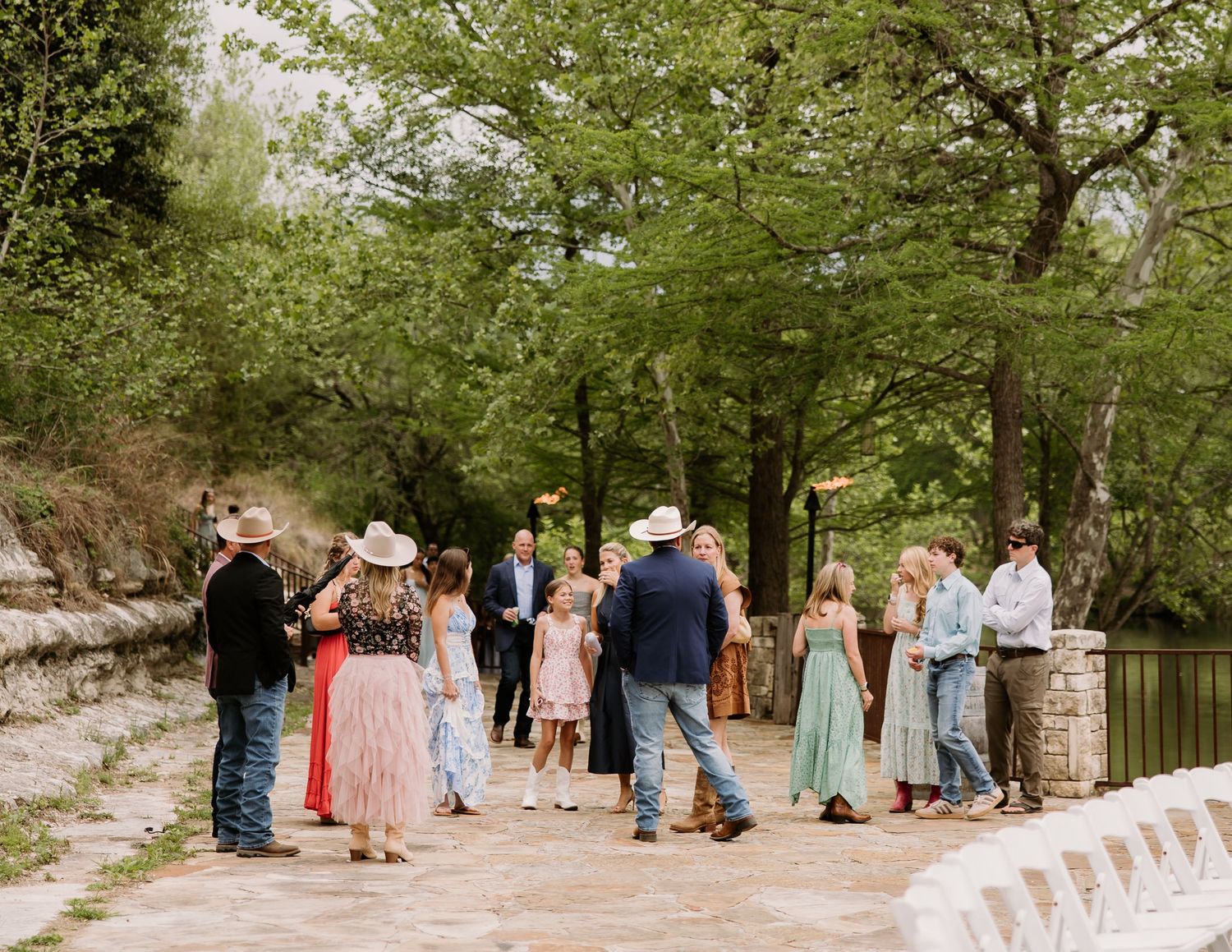 Guests mingle on a stone patio surrounded by lush trees at an outdoor wedding reception.
