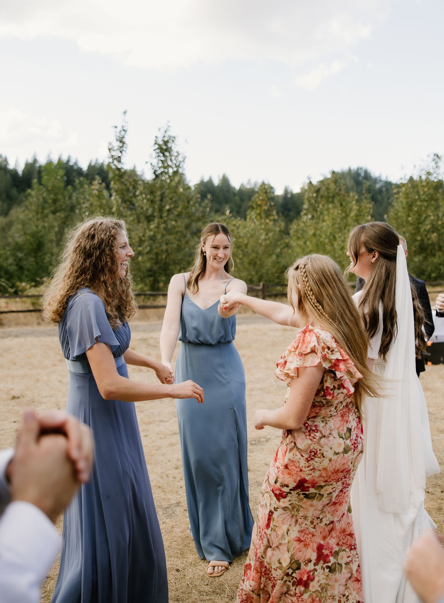 Bridesmaids in blue dresses celebrate with bride in white gown and veil at outdoor wedding.