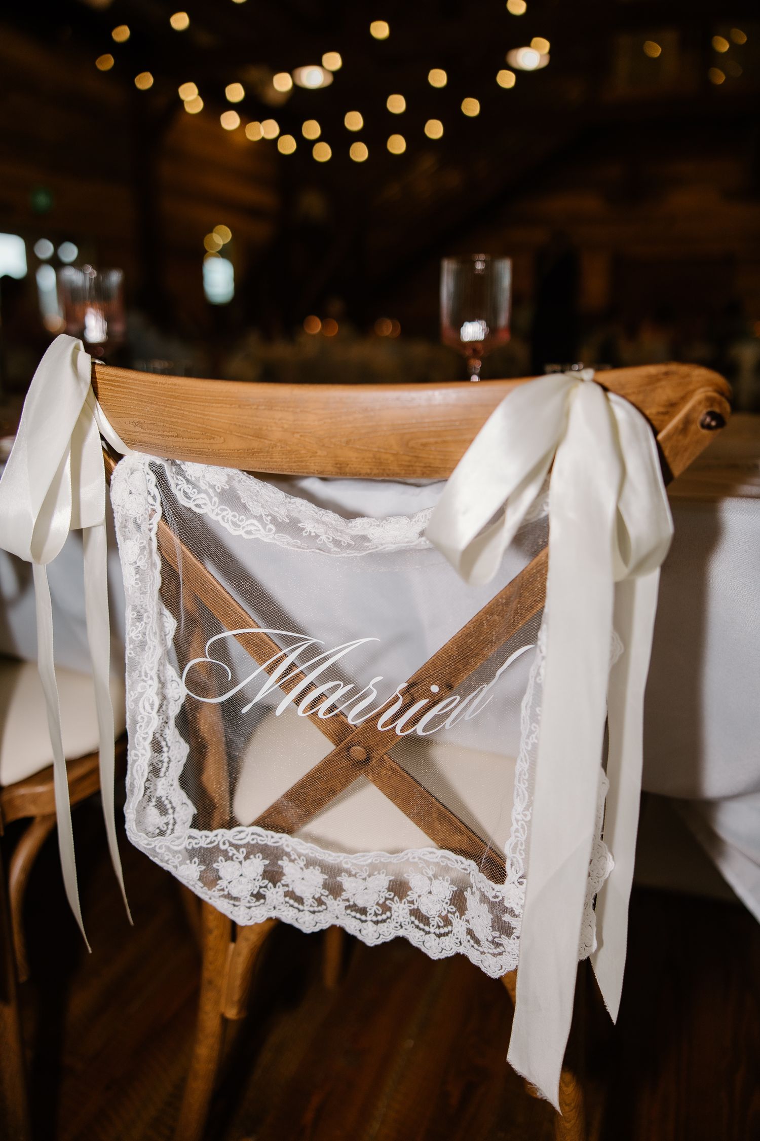 Elegant rustic wooden wedding chair decorated with lace and white ribbon reading Married at reception.