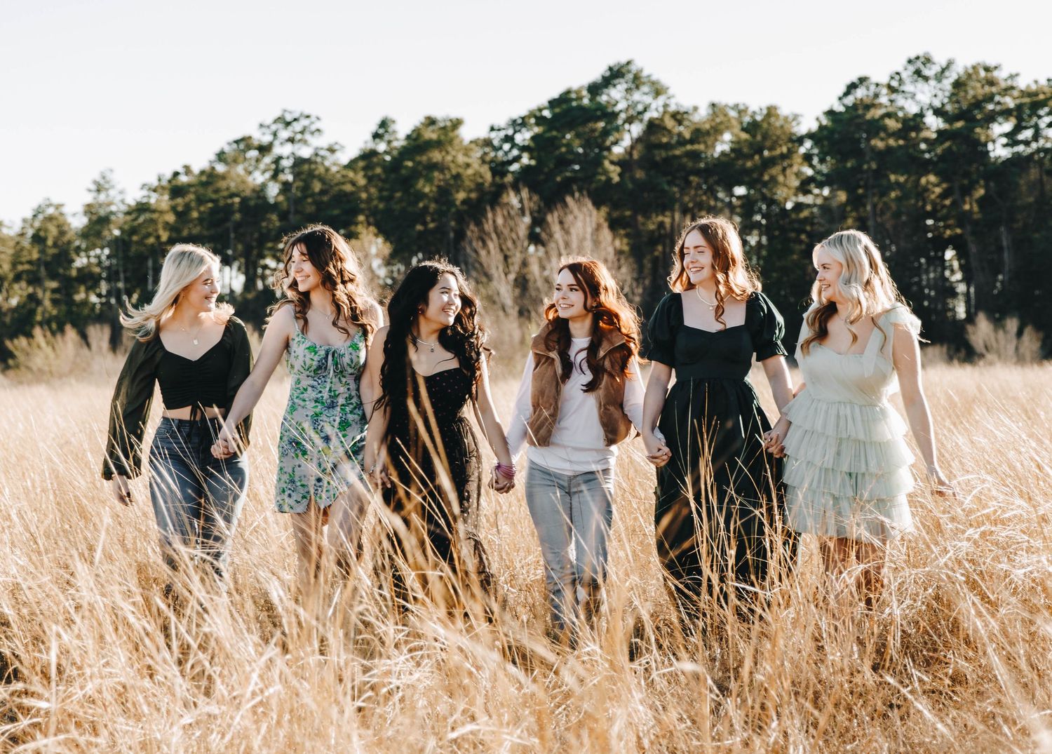 Six young women walking together through a golden field of tall dry grass.