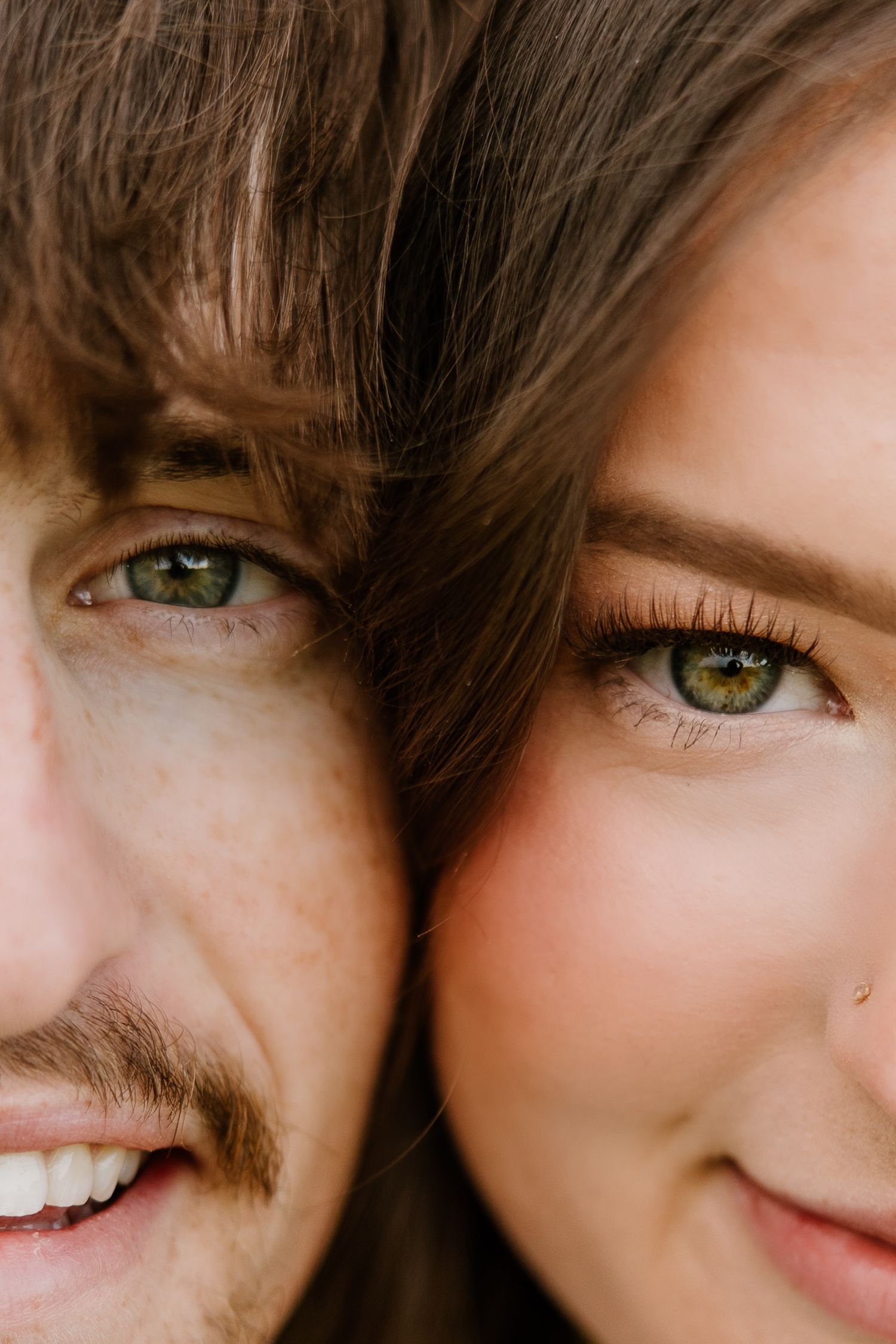Close-up of couple with matching green eyes pressed together, smiling softly.