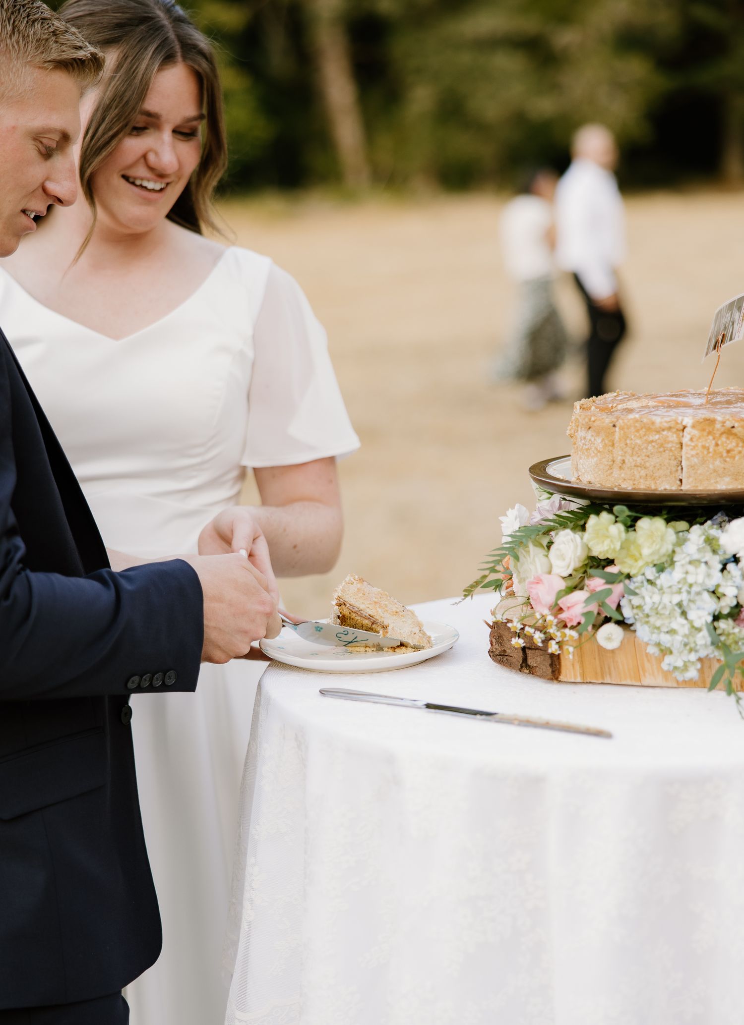 Bride and groom cutting a naked wedding cake outdoors surrounded by lush greenery.