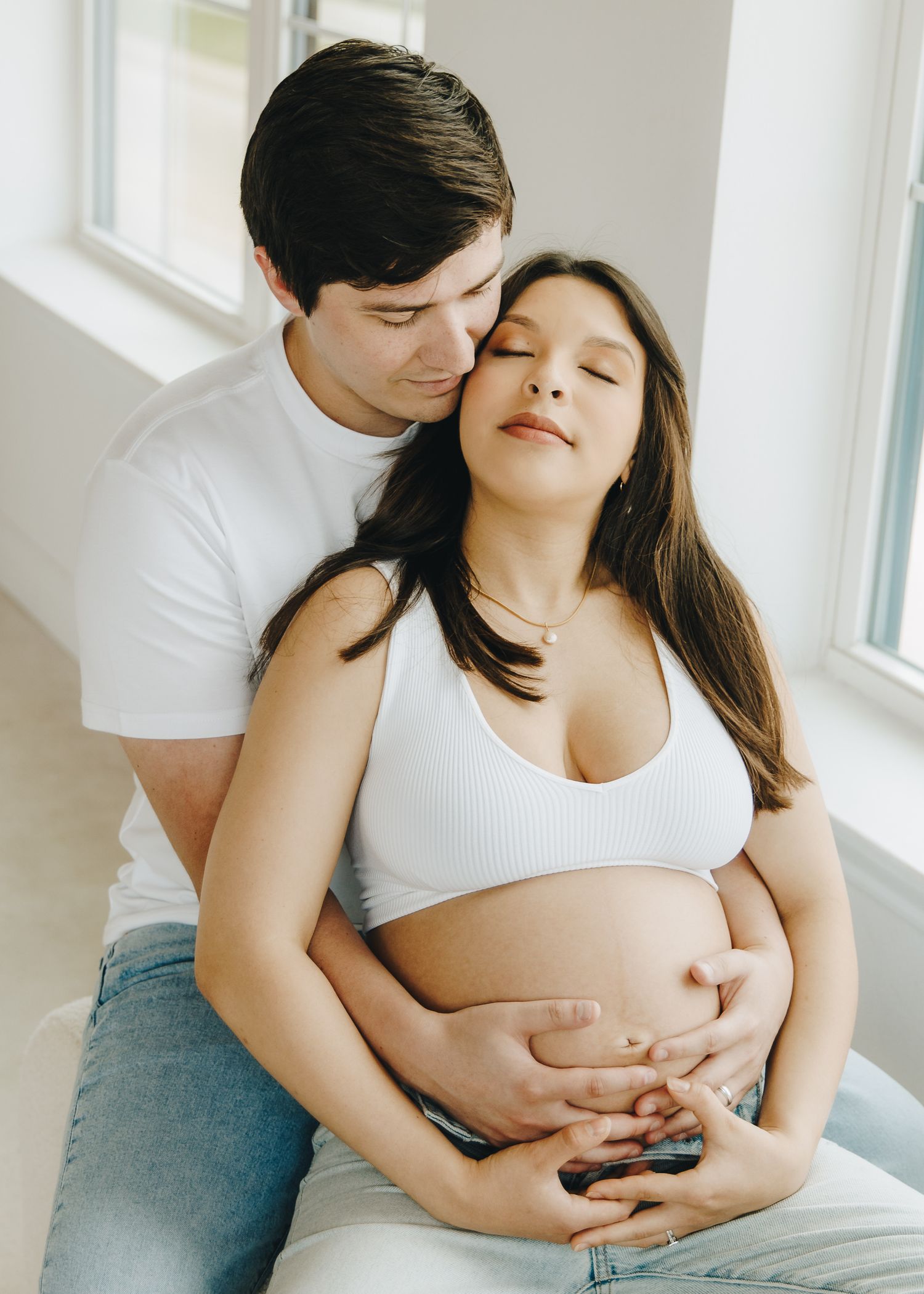 Couple embracing tenderly, man kissing pregnant woman's head as they hold her baby bump.