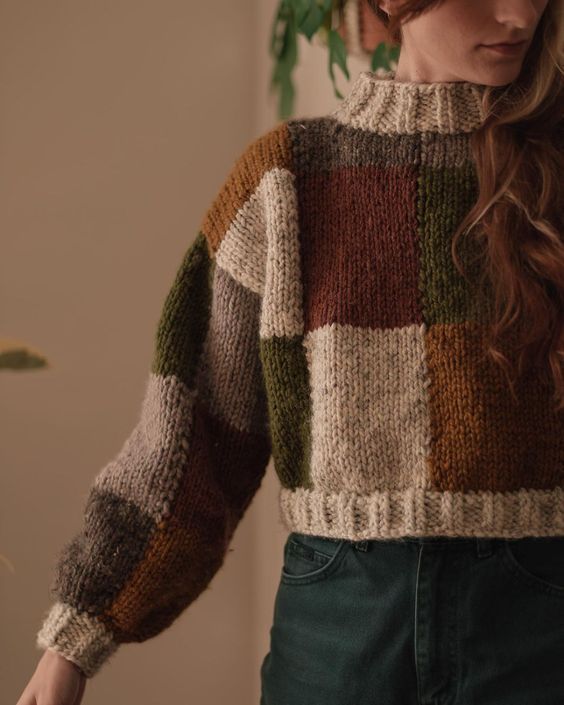 Woman wearing chunky hand-knit color block sweater in earth tones of brown, green, rust, and cream.