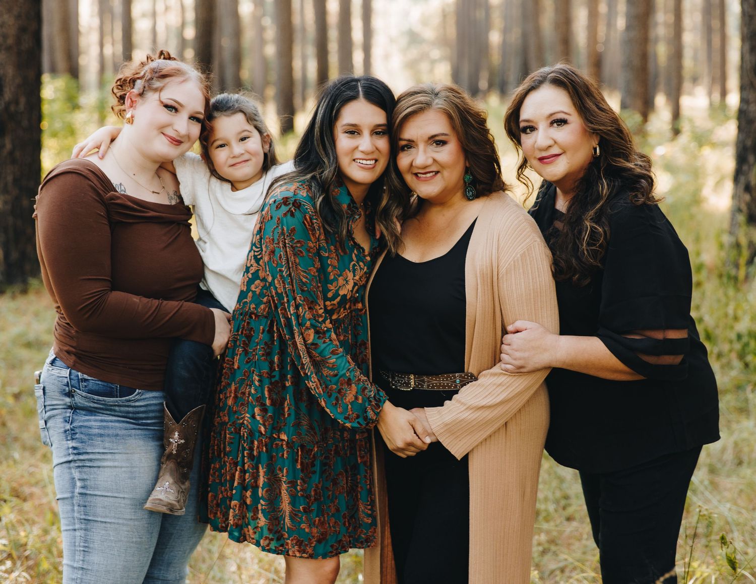 Four women and a young girl pose together smiling in a pine forest during a family portrait session.