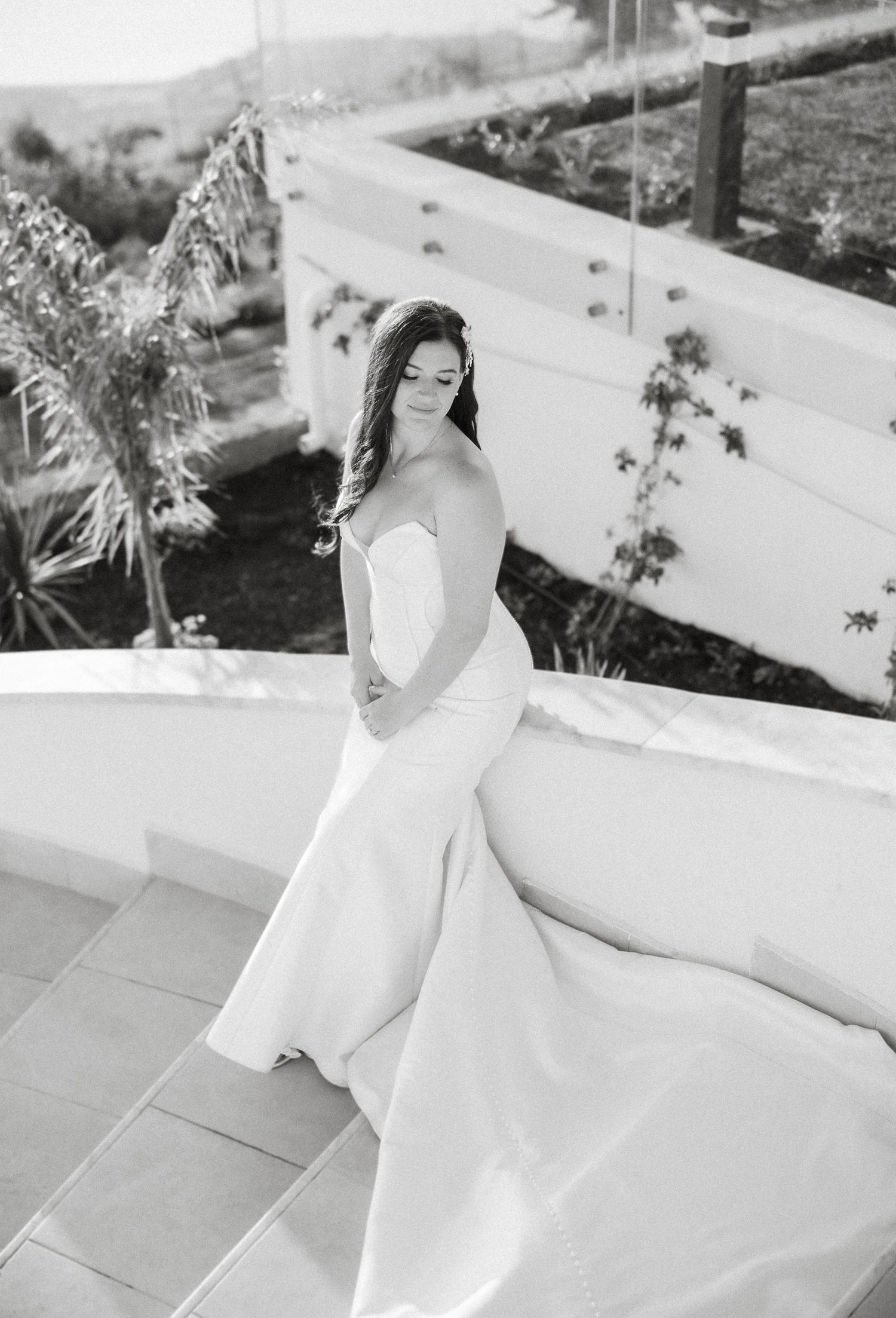 Elegant bride in a strapless mermaid gown poses on a sunlit terrace in a black and white photo.