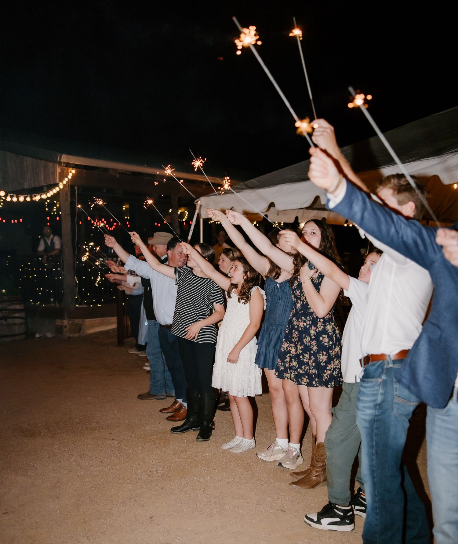 Wedding guests holding sparklers in a line at night creating a glowing send-off tunnel for the newlyweds.