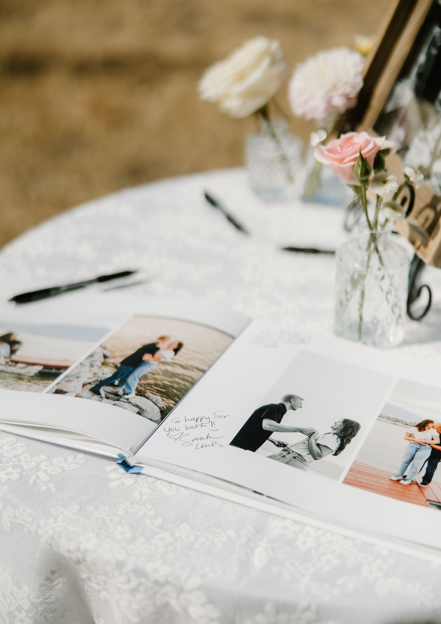Wedding guest book open to couple photos displayed on a white linen table with pink roses.