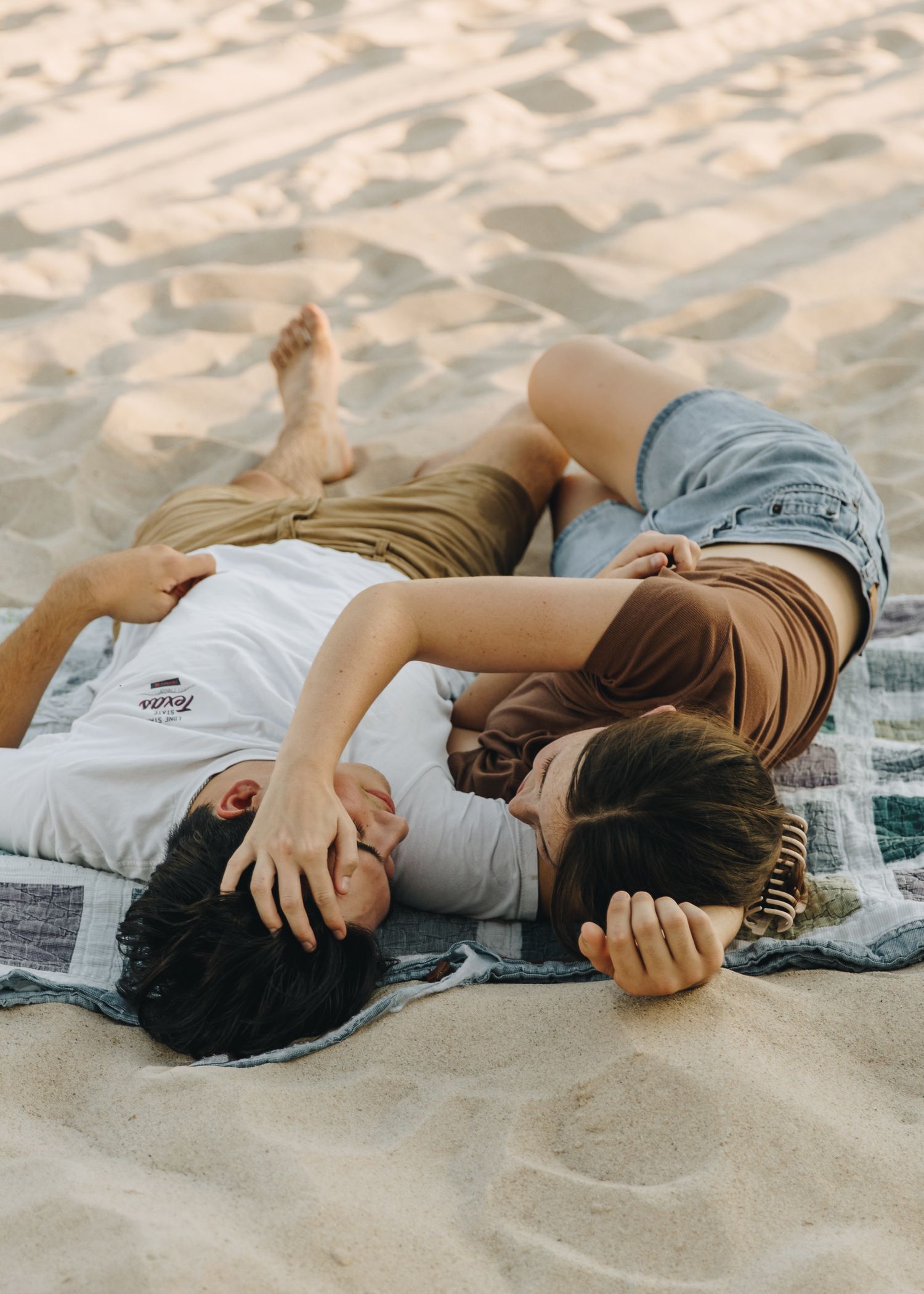 Young couple lying on beach blanket in sand sharing a romantic moment.