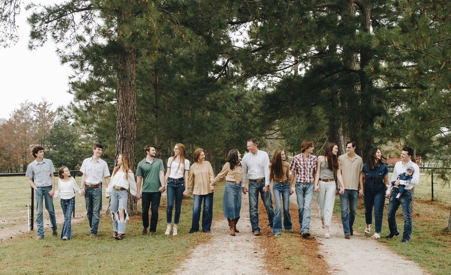 Large extended family walks together along a tree-lined path in a coordinated outdoor portrait.