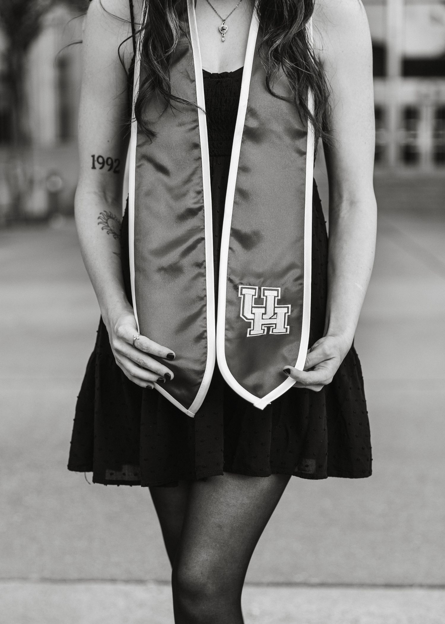 Young woman in black dress wearing University of Houston graduation stole in black and white photo.