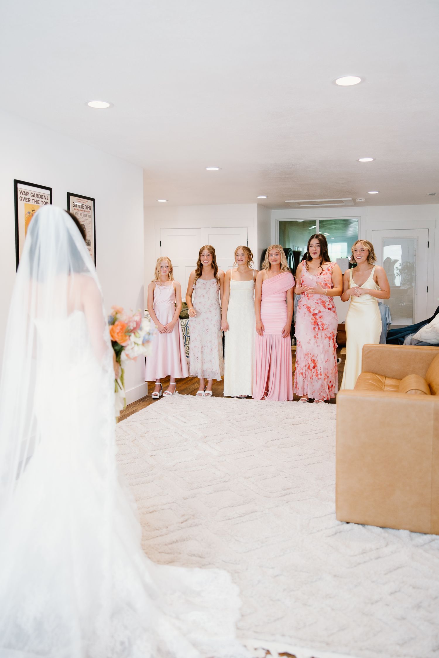 Bride in white gown with veil faces bridesmaids in pink dresses during emotional first look reveal.