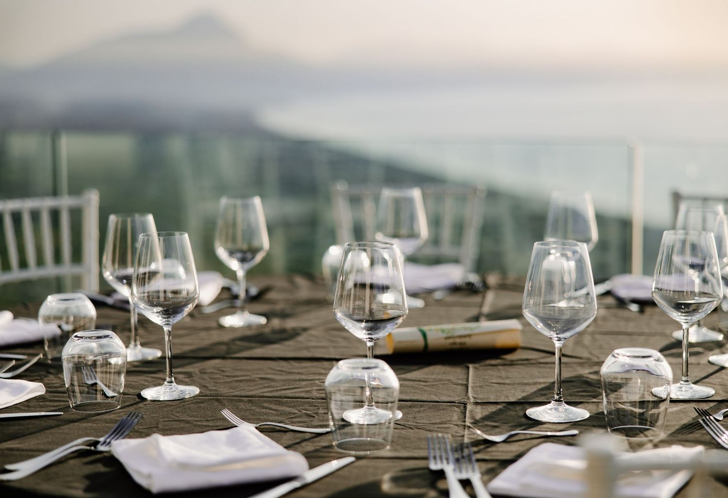 Elegant outdoor wedding reception table set with crystal wine glasses overlooking a scenic coastal view.