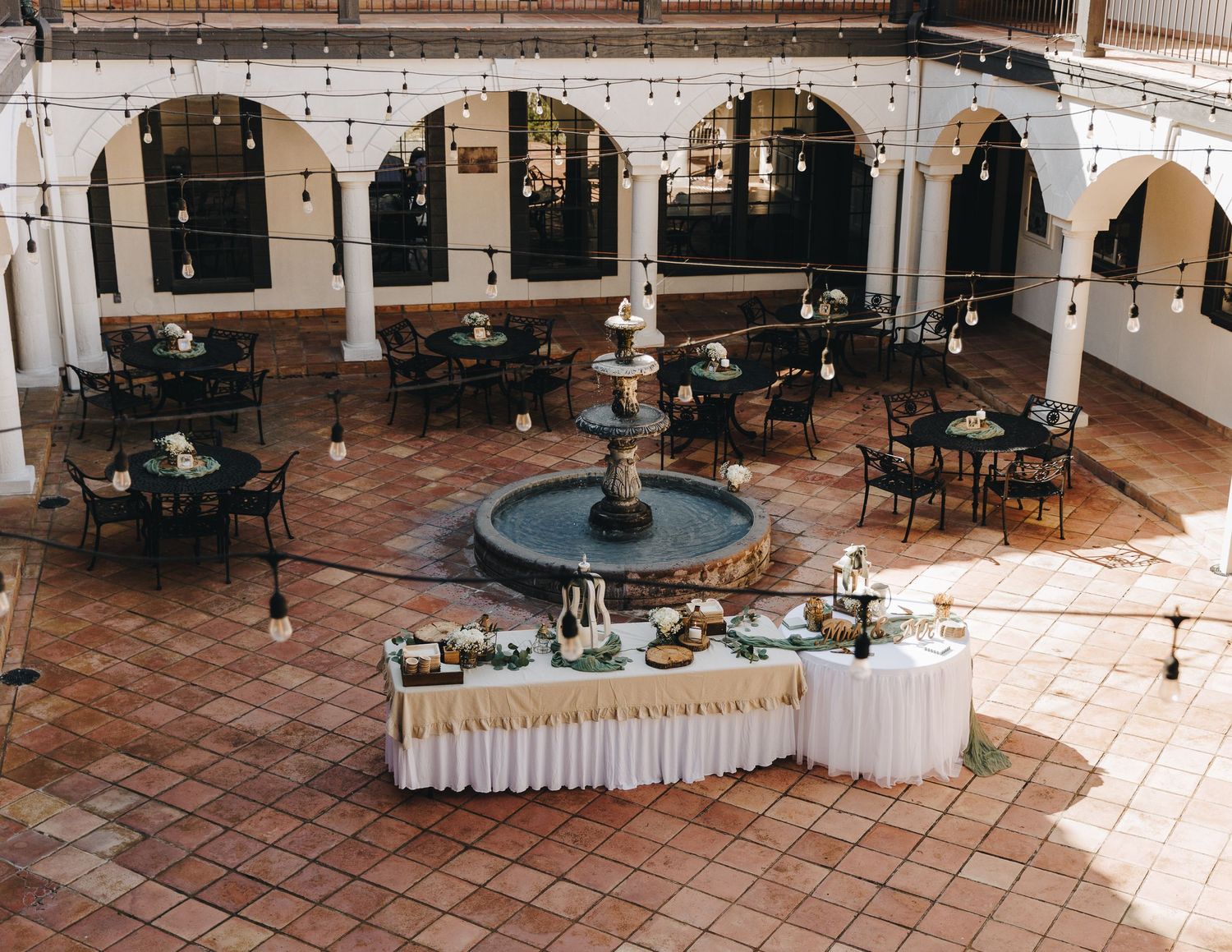 Aerial view of wedding venue courtyard with fountain, tables, and string lights.