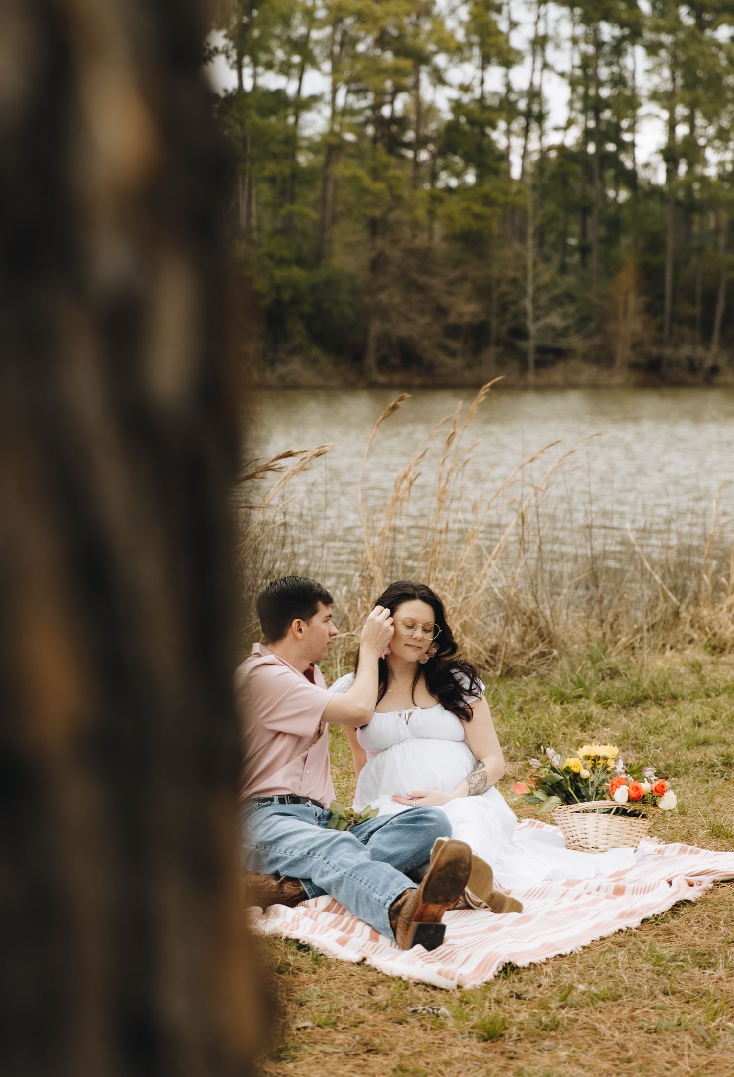 Expectant couple sitting on blanket near lake during romantic outdoor maternity photography session.