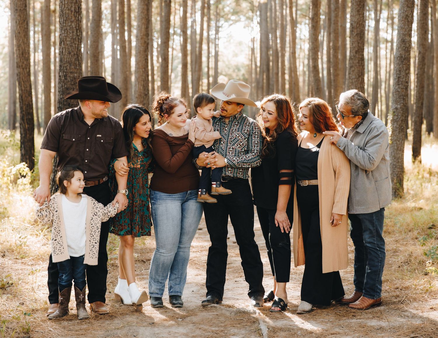 Extended multigenerational family gathered together on sunlit pine forest path.